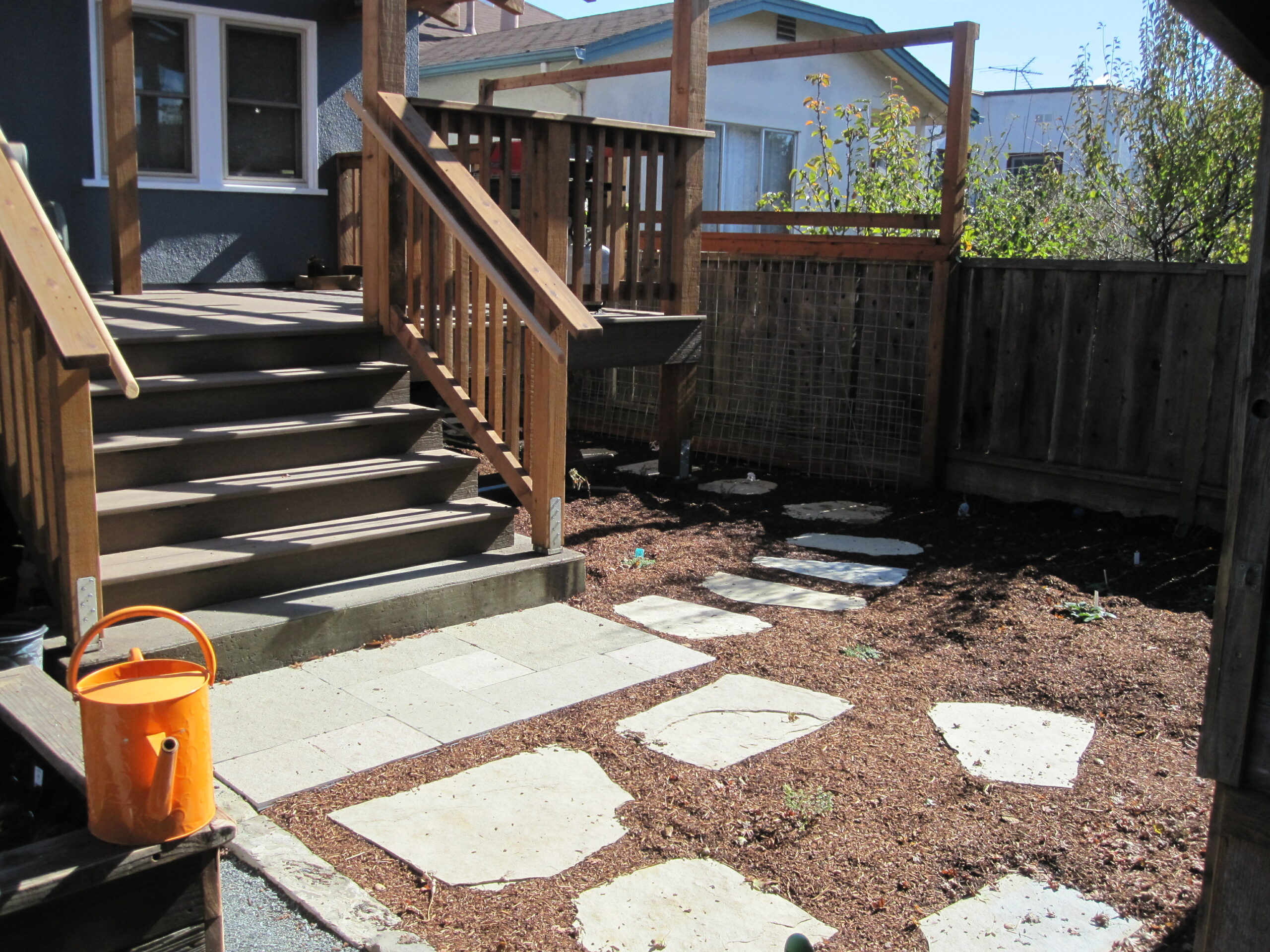 Backyard with deck access via wooden stairs, stone paver walkway, mulch landscaping, and a privacy wood fence along the perimeter.