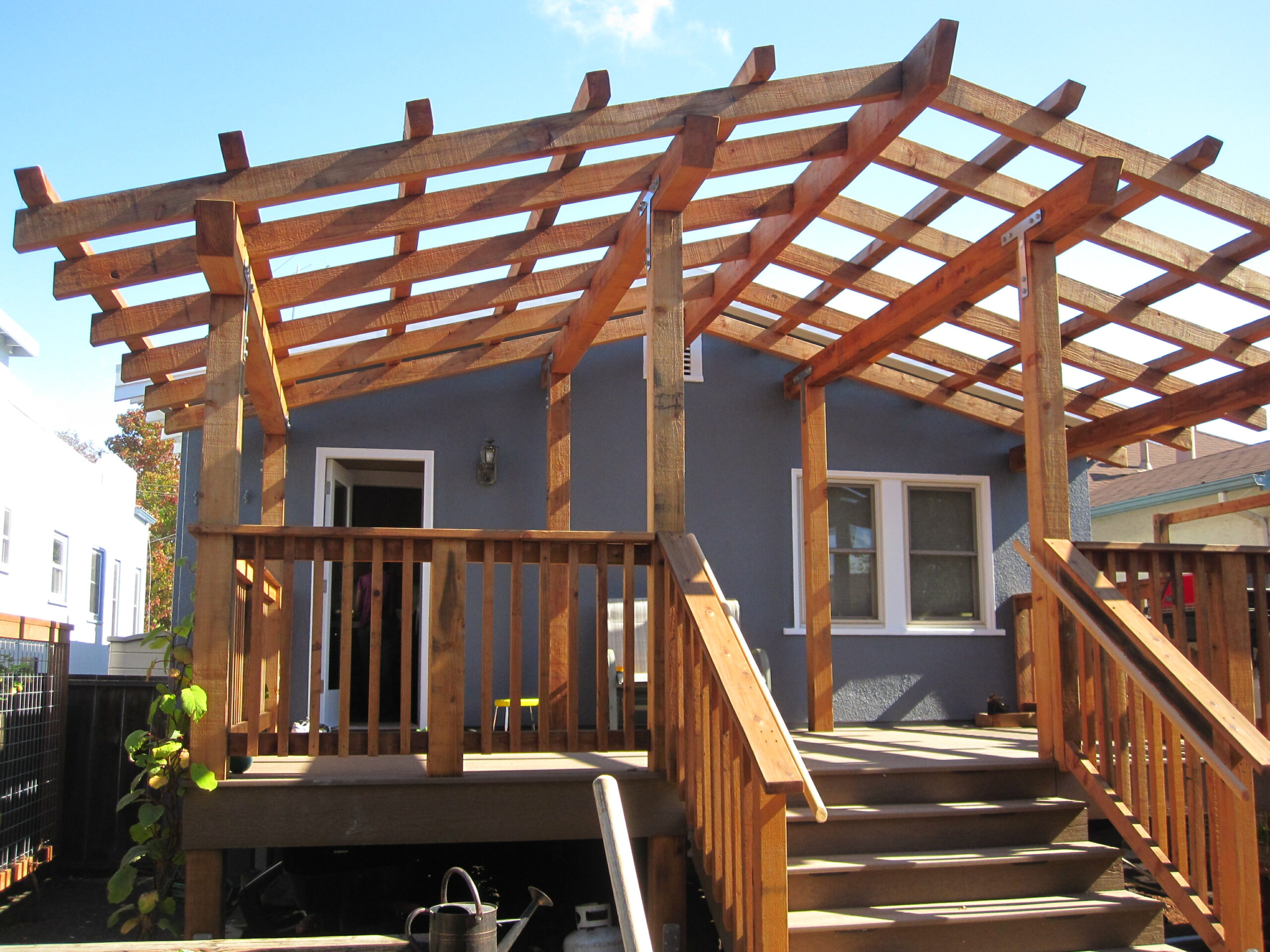 Deck with stairs and railing provides entry to house; overhead, a partially built pergola shows potential for outdoor upgrades.