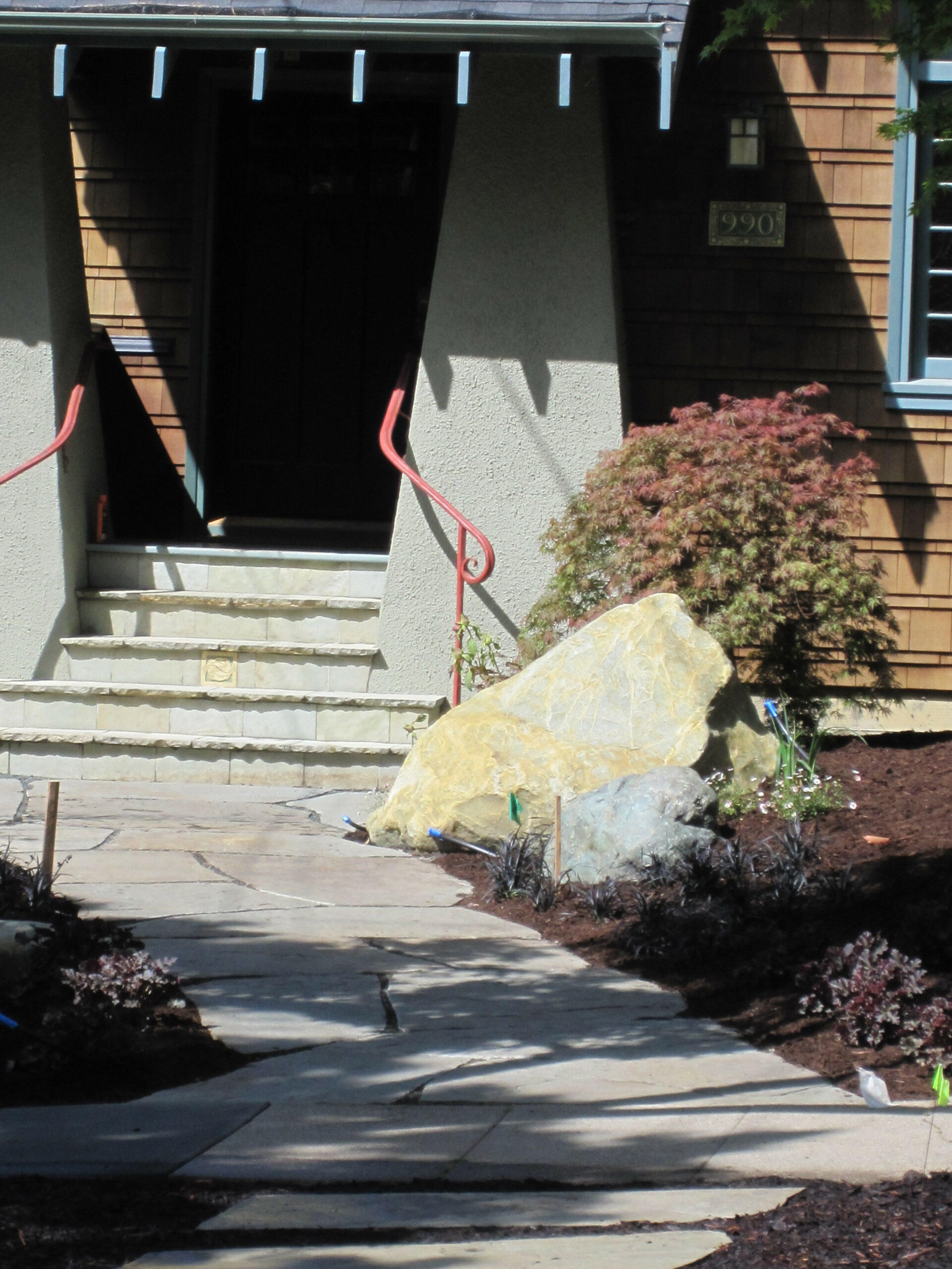 Stone walkway to entry steps with sturdy handrails; landscaped front yard includes hardscape elements and low-maintenance planting.