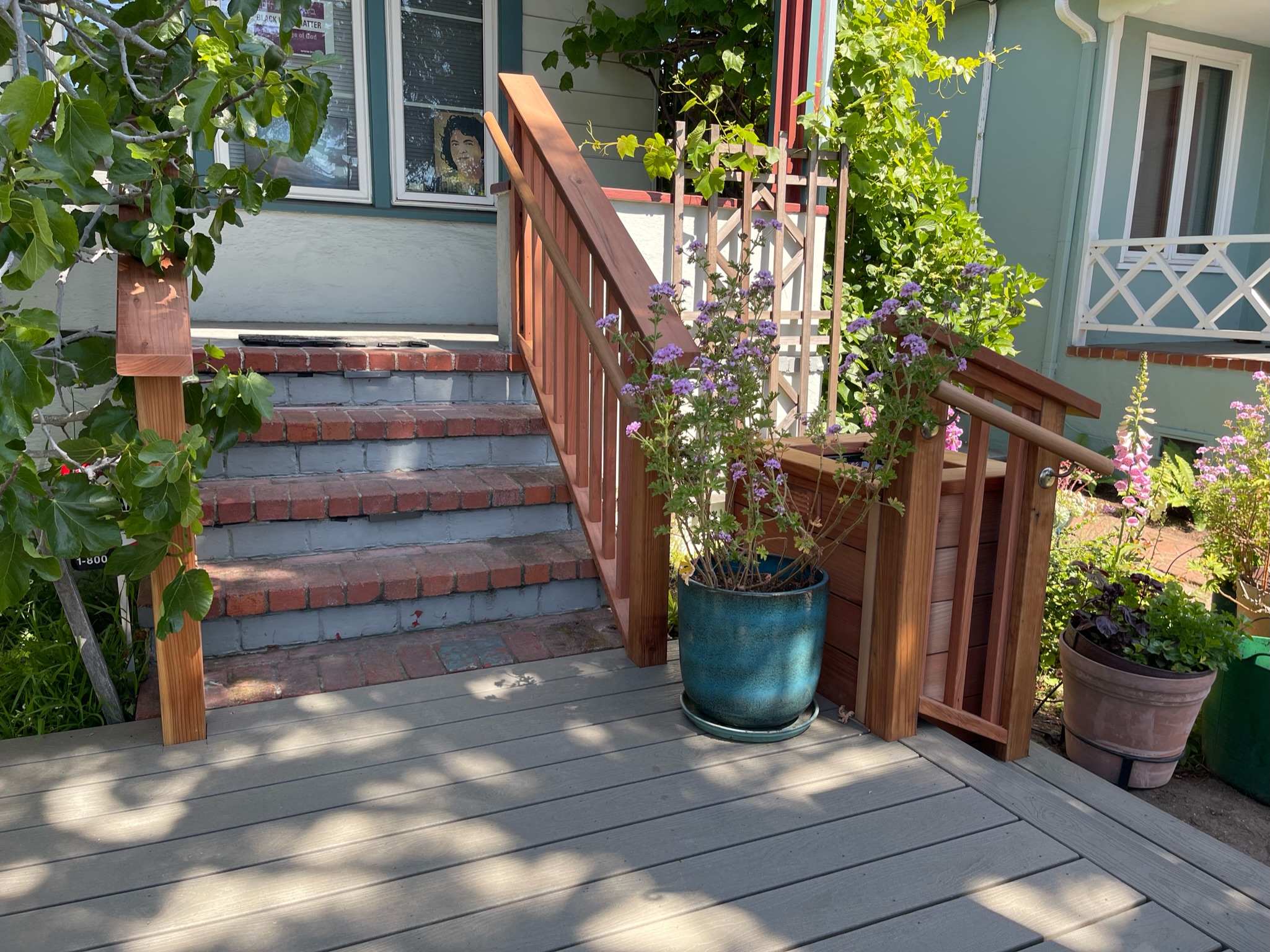 Front deck with wooden steps, railing, and large windows; ample natural light and mature landscaping offer redevelopment potential.