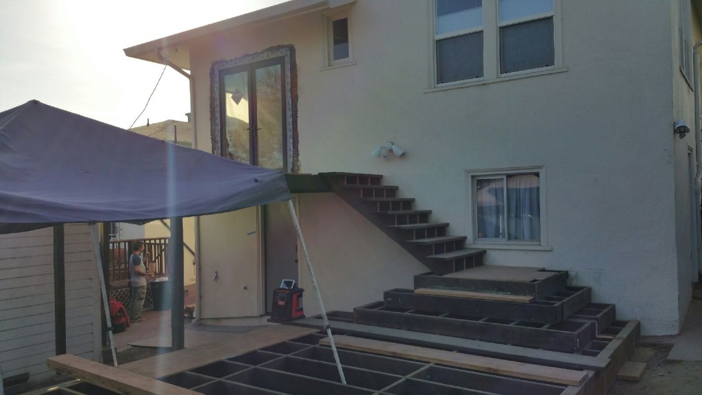 Two-story Rockridge home showing in-progress cascading deck and stair build; temporary canopy covers active construction zone.