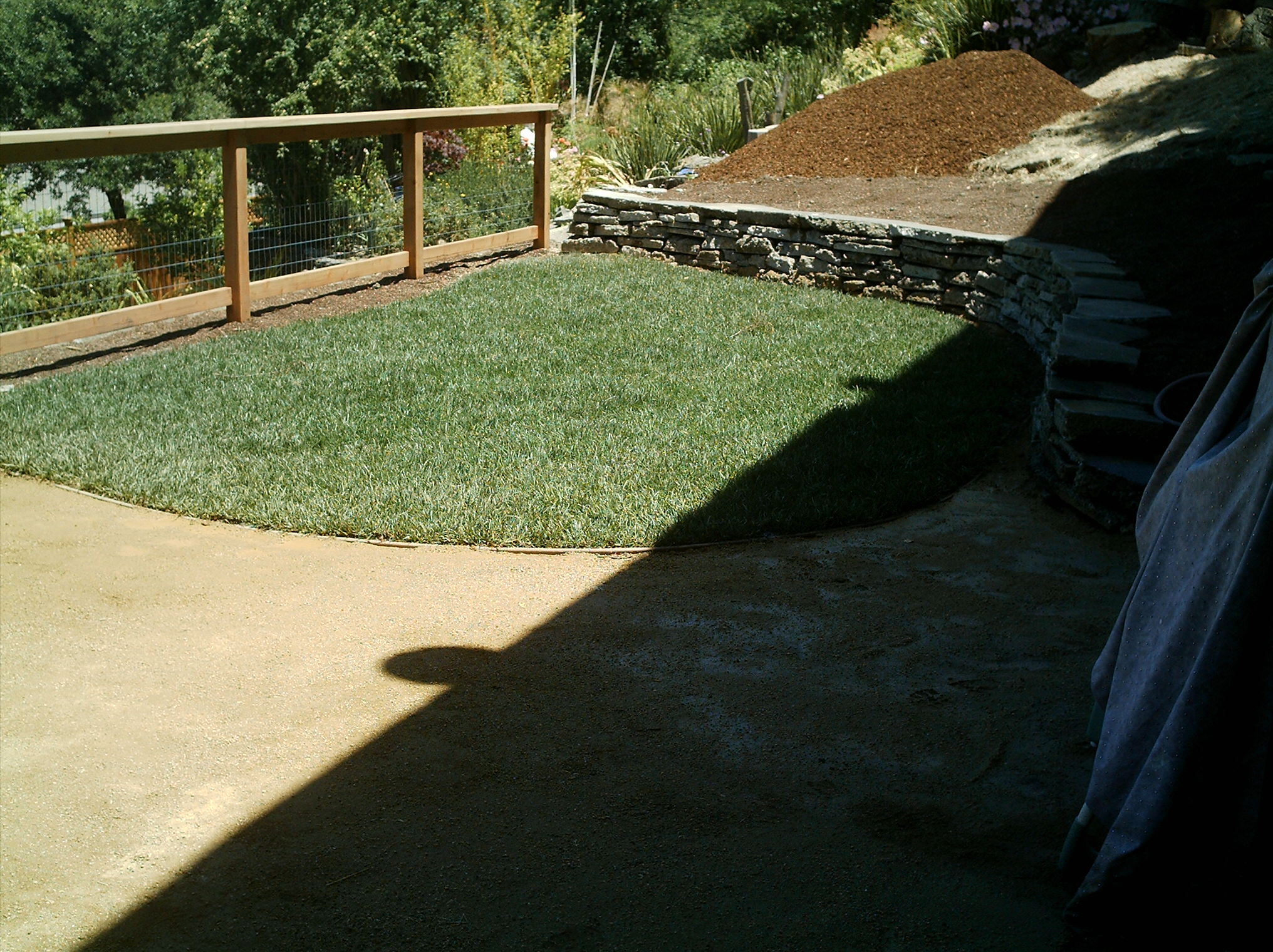 Crocker Highlands backyard featuring usable lawn, stone retaining wall for grading, wood fencing, dirt area, and mulch pile.