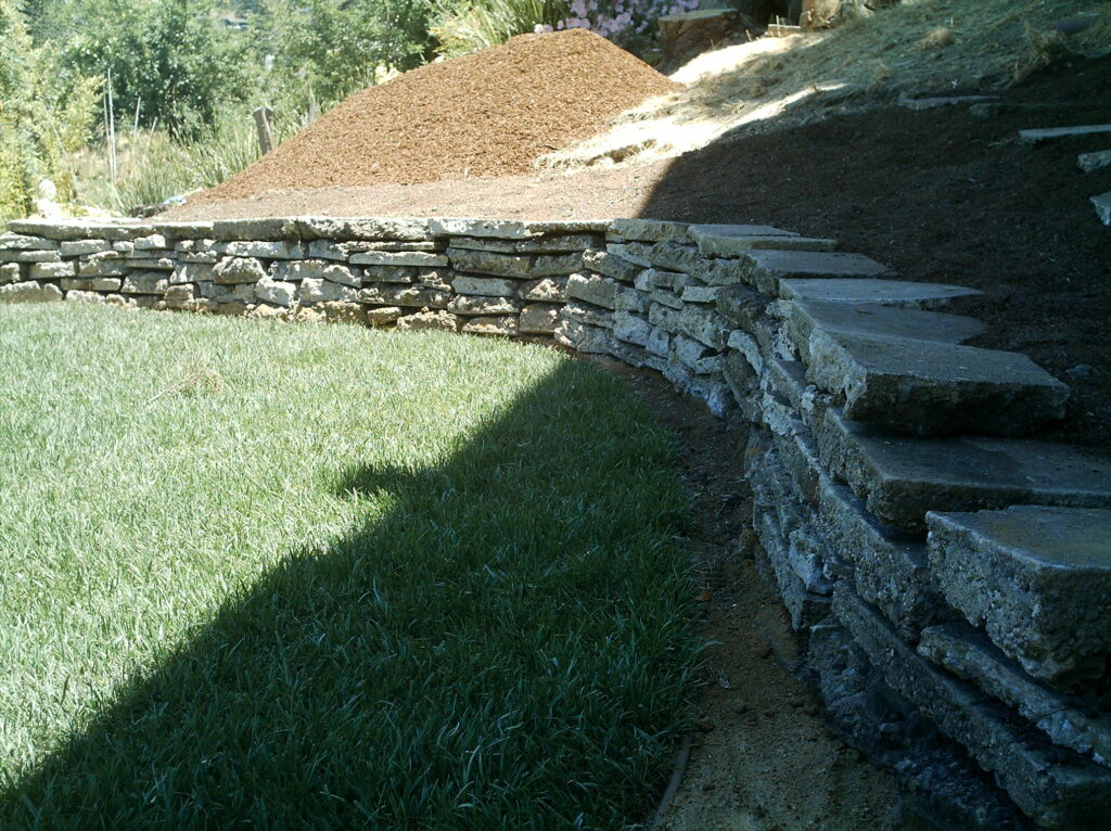 Curved stone retaining wall defines backyard edge, offering erosion control and potential for tiered landscaping in Crocker Highlands.