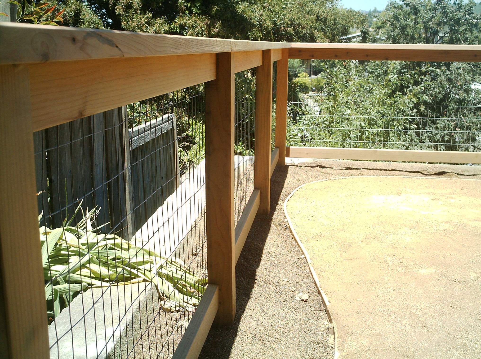 Enclosed dirt area adjacent to garden bed offers potential for landscaping or expansion; mature trees provide privacy in backyard.