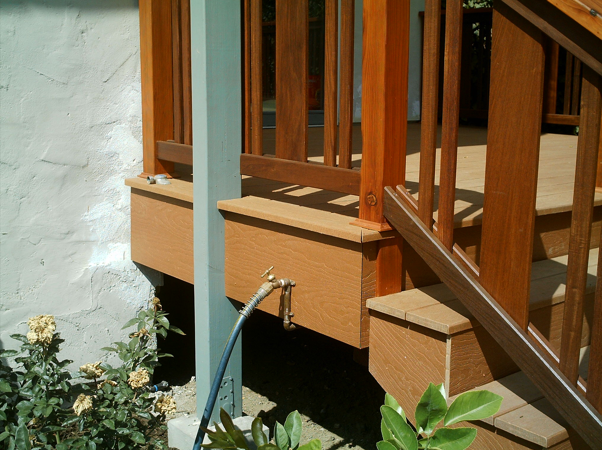 Outdoor faucet plumbed into a sturdy Elmwood deck, hose access nearby; landscaping is established at the base of the porch.