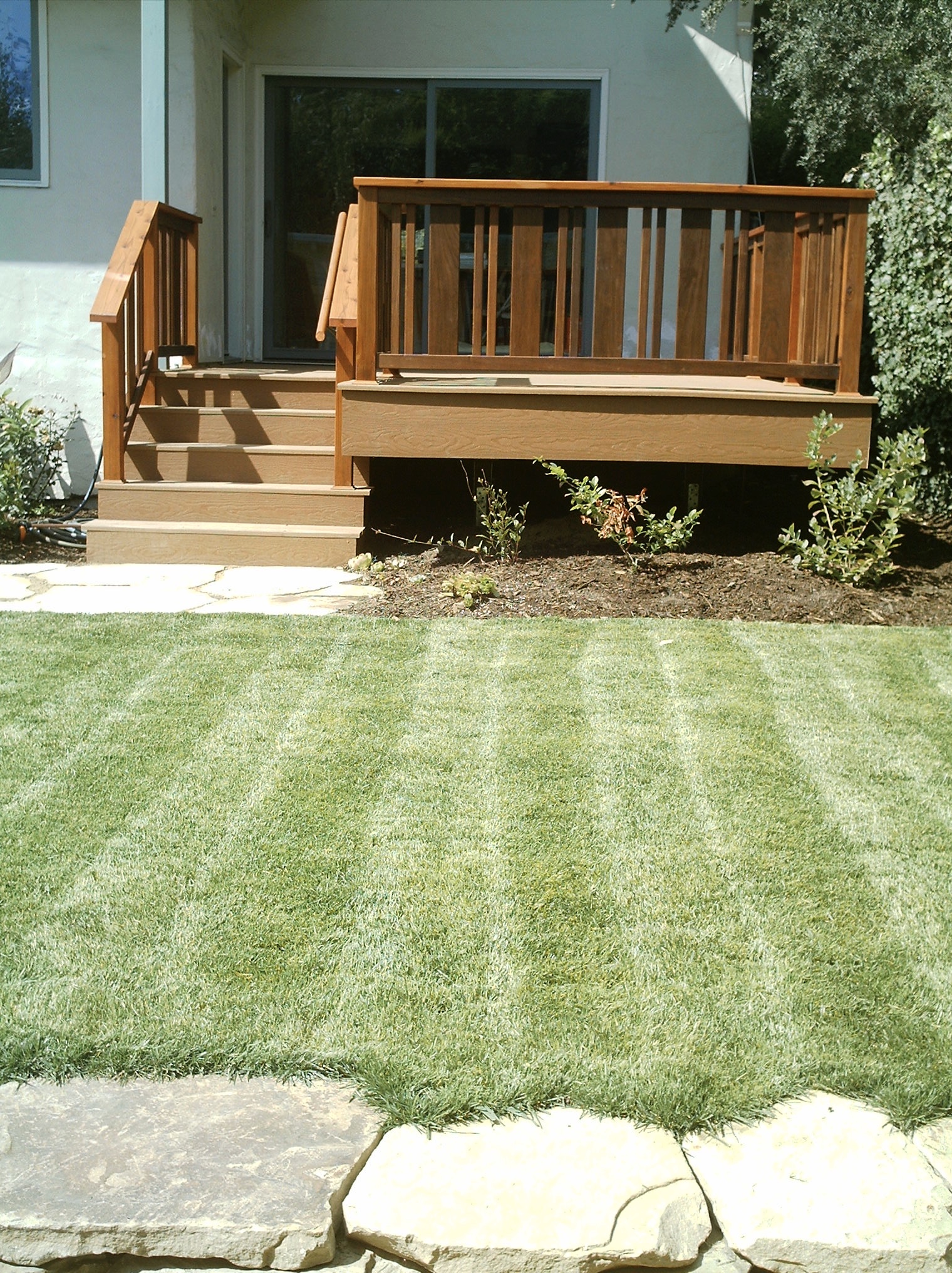 Deck with stairs offers direct access to the home’s interior through a sliding glass door; front yard features organized hardscaping.