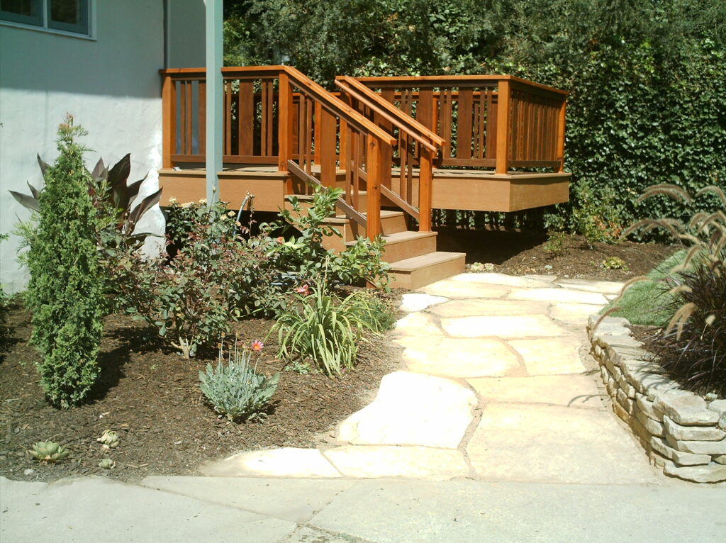 Deck with stairs offers outdoor access to a stone walkway, featuring low-maintenance landscaping and a small retaining wall.