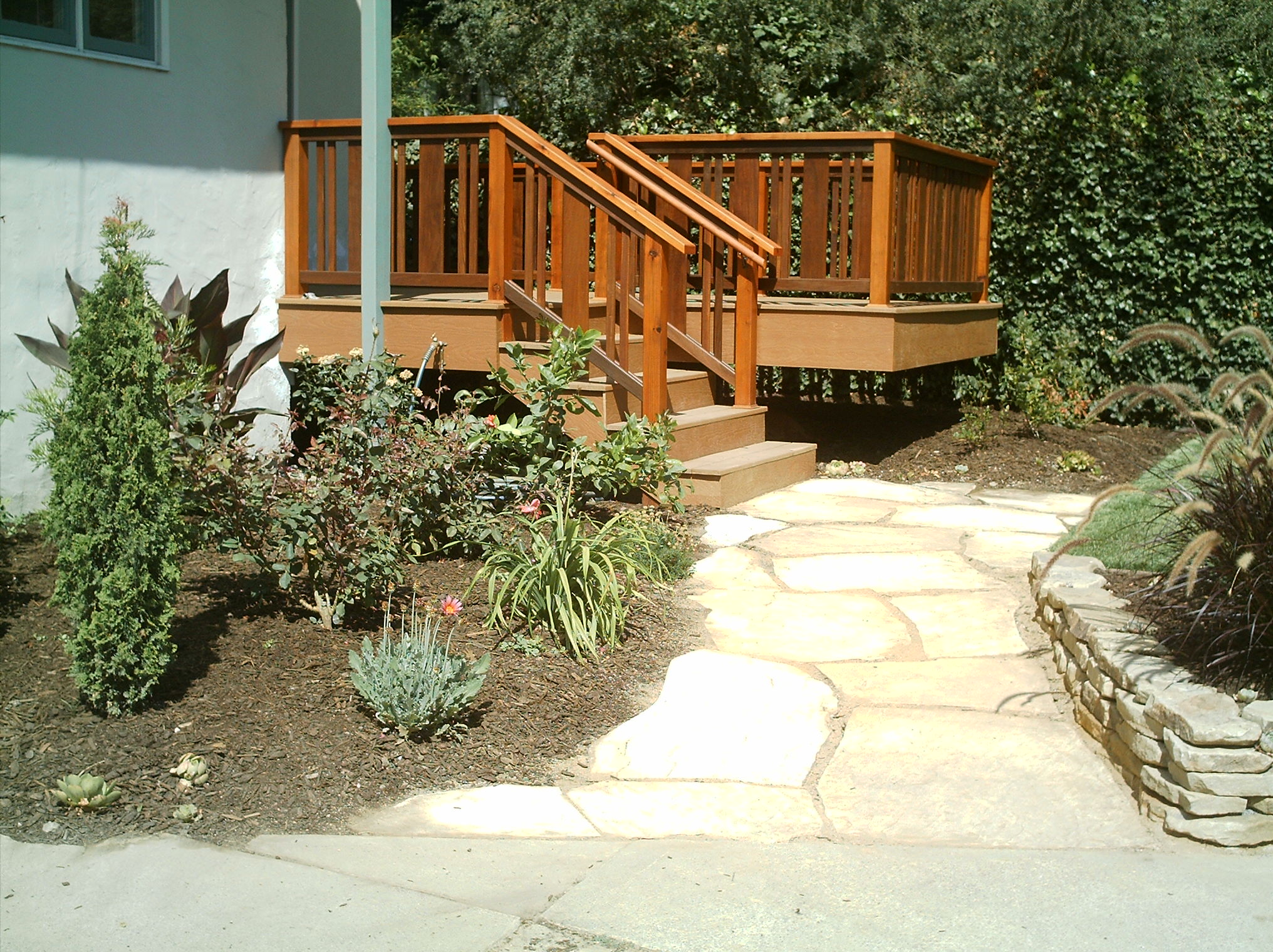 Deck with stairs offers outdoor access to a stone walkway, featuring low-maintenance landscaping and a small retaining wall.