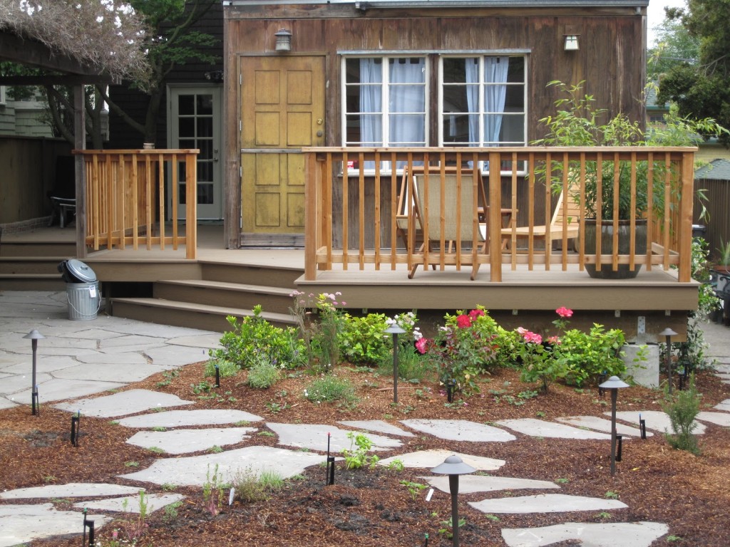 Spacious deck with sturdy railings, direct garden access via stone path, low-maintenance landscaping and durable hardscape elements.