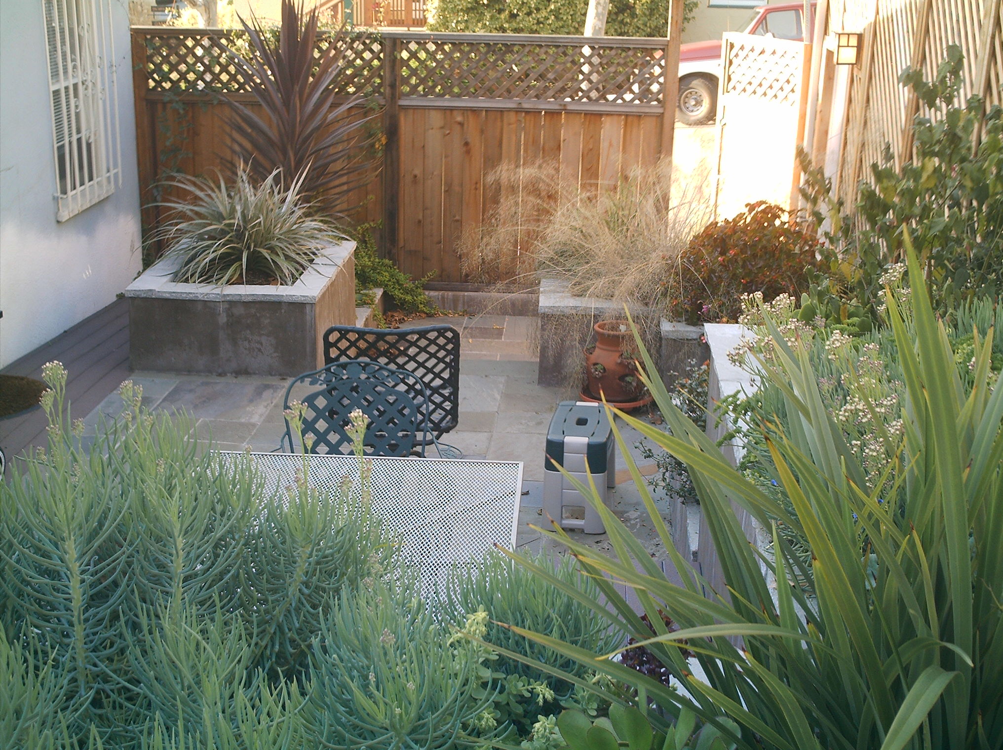 Backyard patio near Grand Lake with raised planters, mature greenery, and privacy fence, offering strong redevelopment potential.