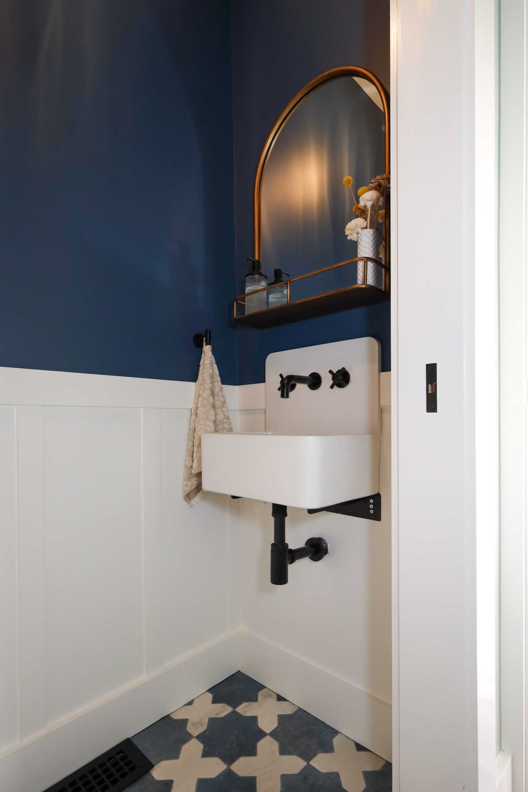 Compact bathroom corner featuring wall-mounted sink, efficient fixtures, space-saving shelf, and durable tile flooring.