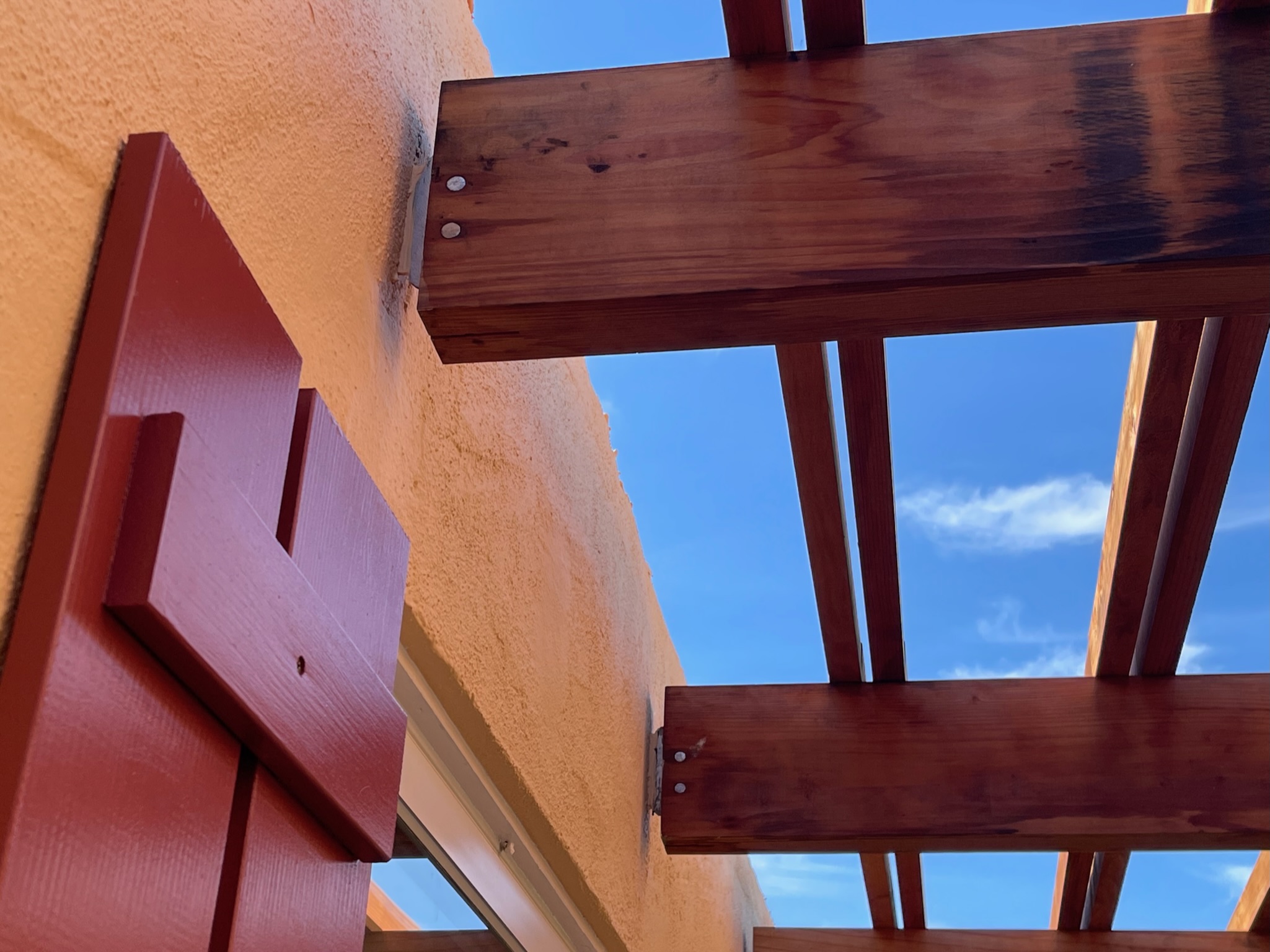 Structural wooden beams support a pergola above a stucco wall and window, suggesting solid framework and outdoor upgrade potential.