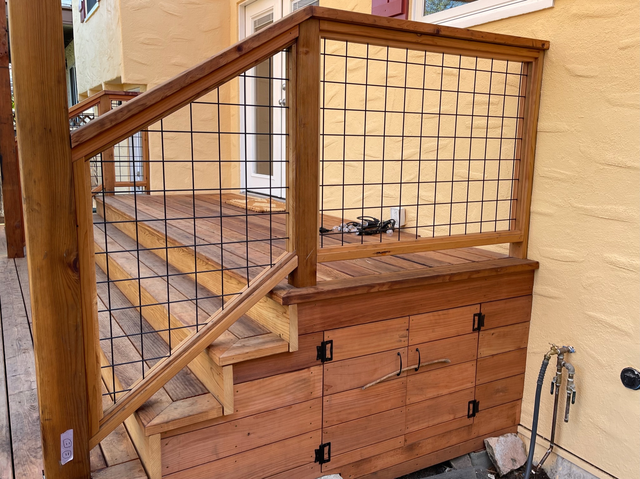 North Albany Deck shows deck stairs with wire railing, built-in under-stair storage, and wall-mounted exterior water access.