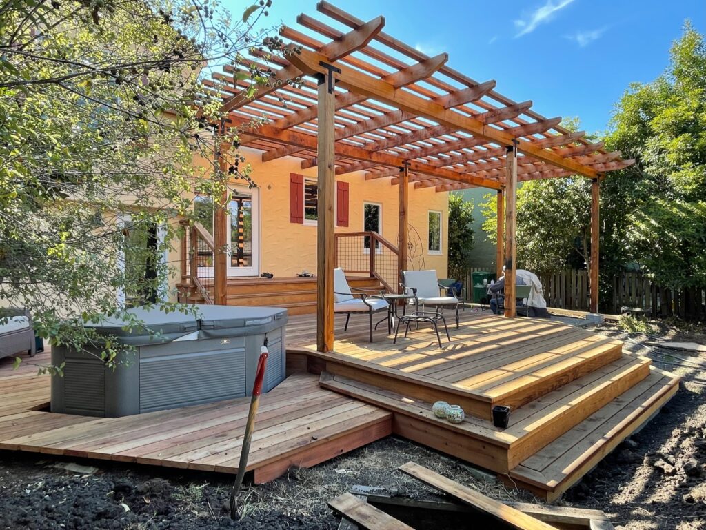 A North Albany backyard deck with a pergola and hot tub connects to steps leading to a partially developed garden area.