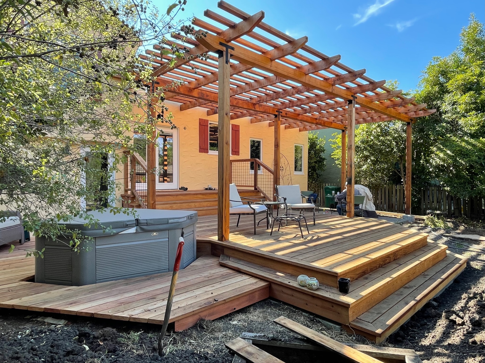 A North Albany backyard deck with a pergola and hot tub connects to steps leading to a partially developed garden area.