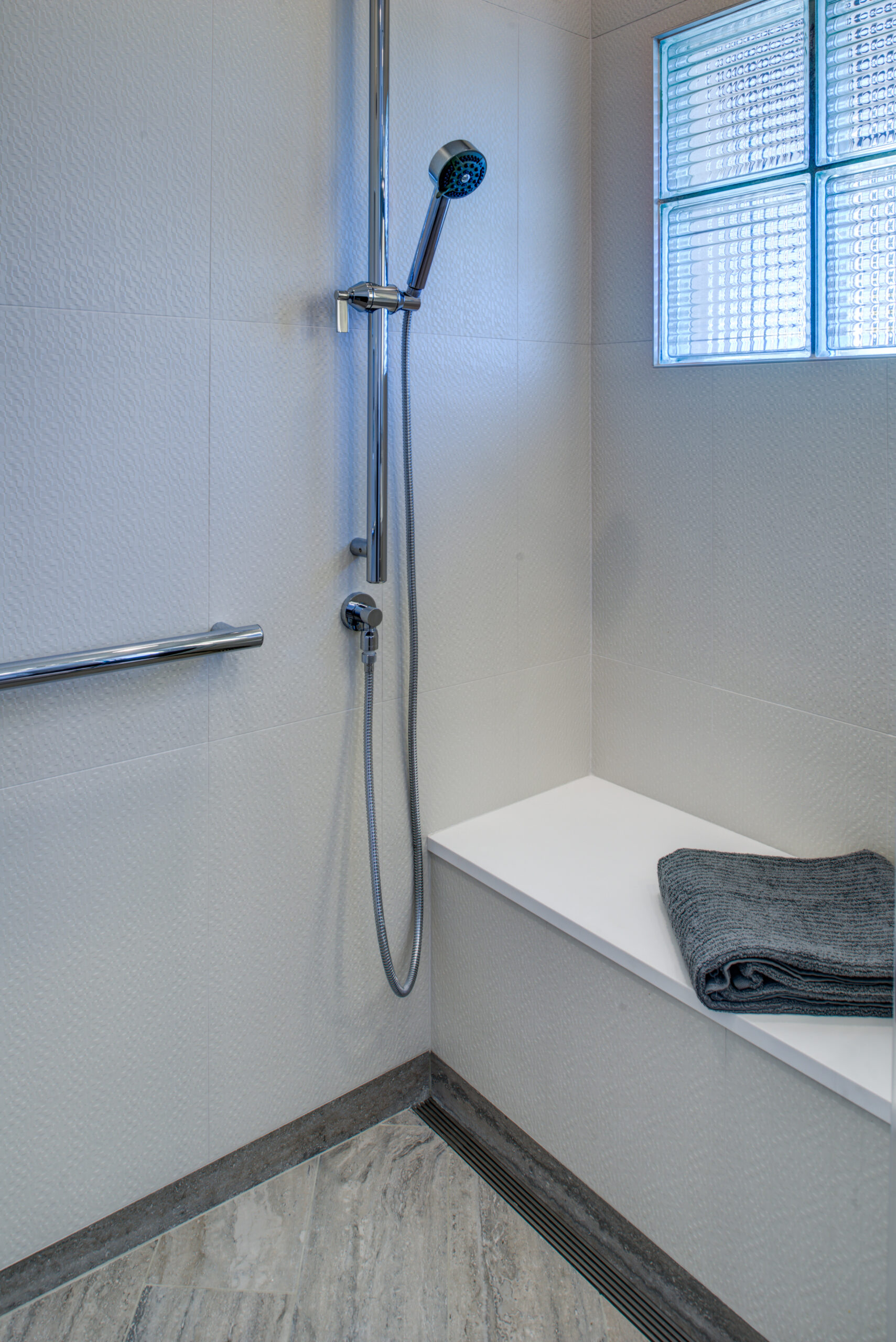 Bathroom includes accessibility upgrades: a handheld showerhead, horizontal grab bar, and built-in bench for added functionality.