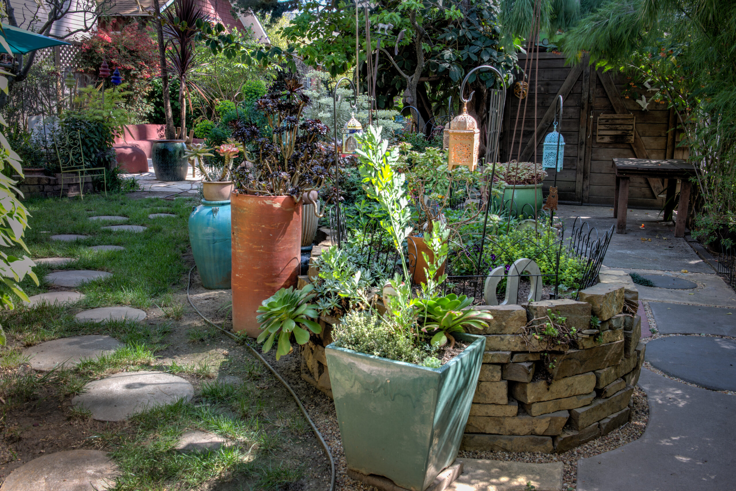 North Oakland backyard with established hardscaping, mature planting beds, a stone walkway, and existing wooden storage shed.