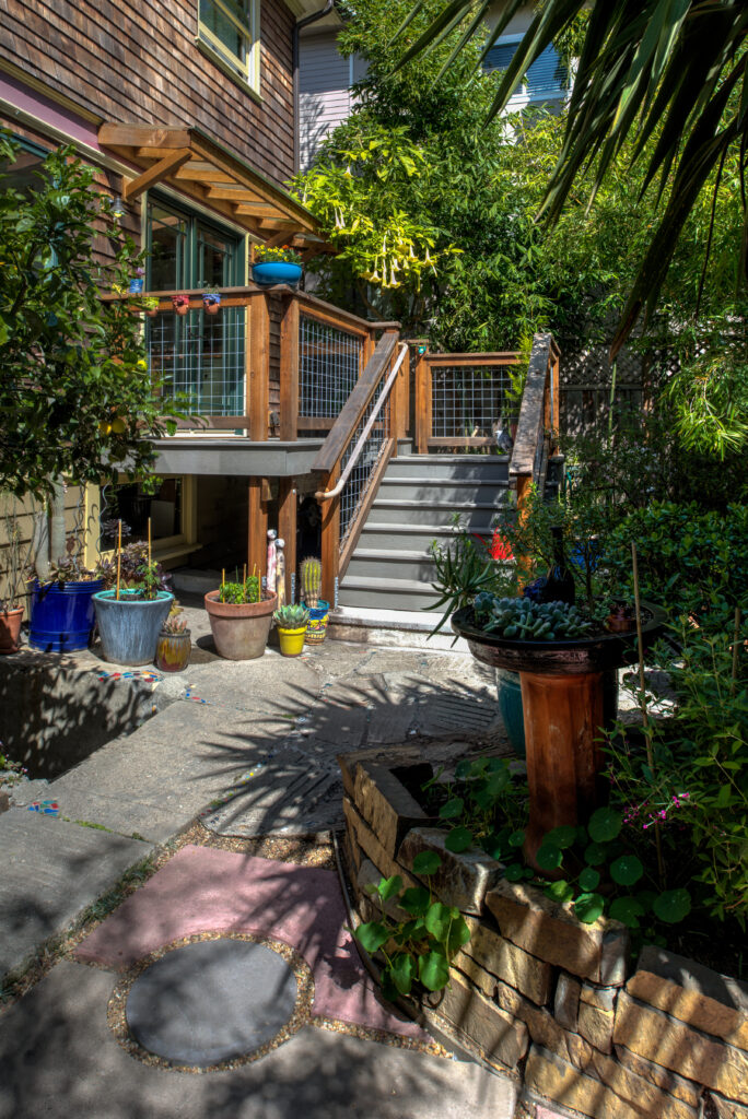 Backyard in North Oakland featuring a raised deck with stairs, stone pathway, and mature landscaping ideal for redevelopment.