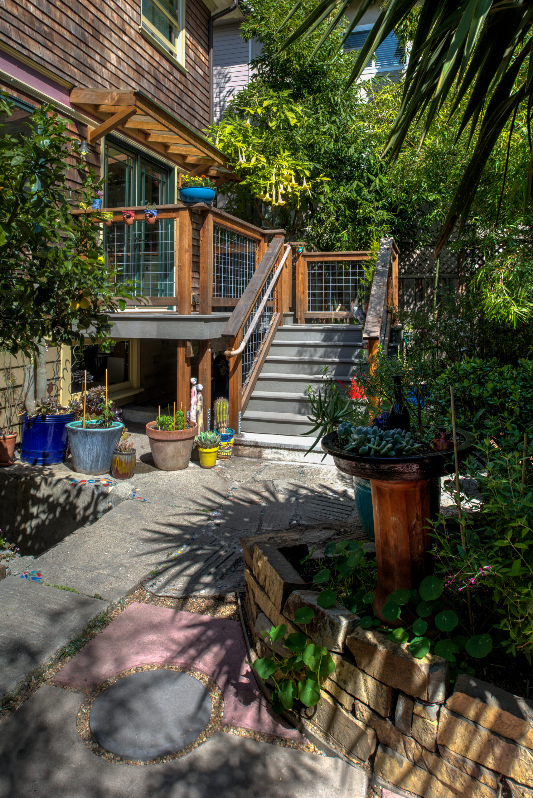 Backyard in North Oakland featuring a raised deck with stairs, stone pathway, and mature landscaping ideal for redevelopment.