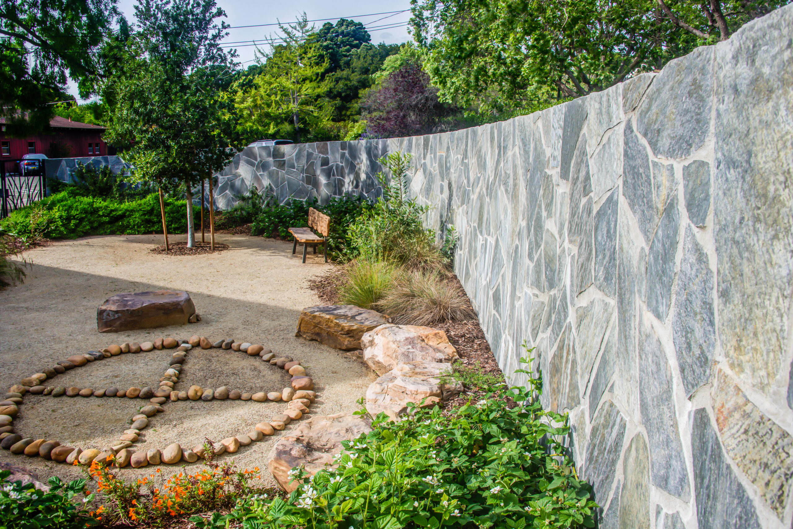 A landscaped garden with low-maintenance gravel, mature trees, and a substantial stone wall offering privacy and structural interest.