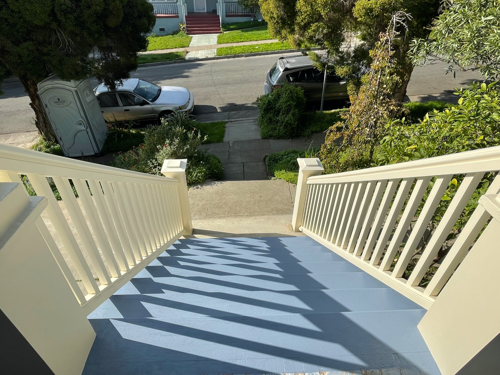 View from the top of a sturdy outdoor staircase overlooking a spacious front yard, sidewalk, and street in a residential area.