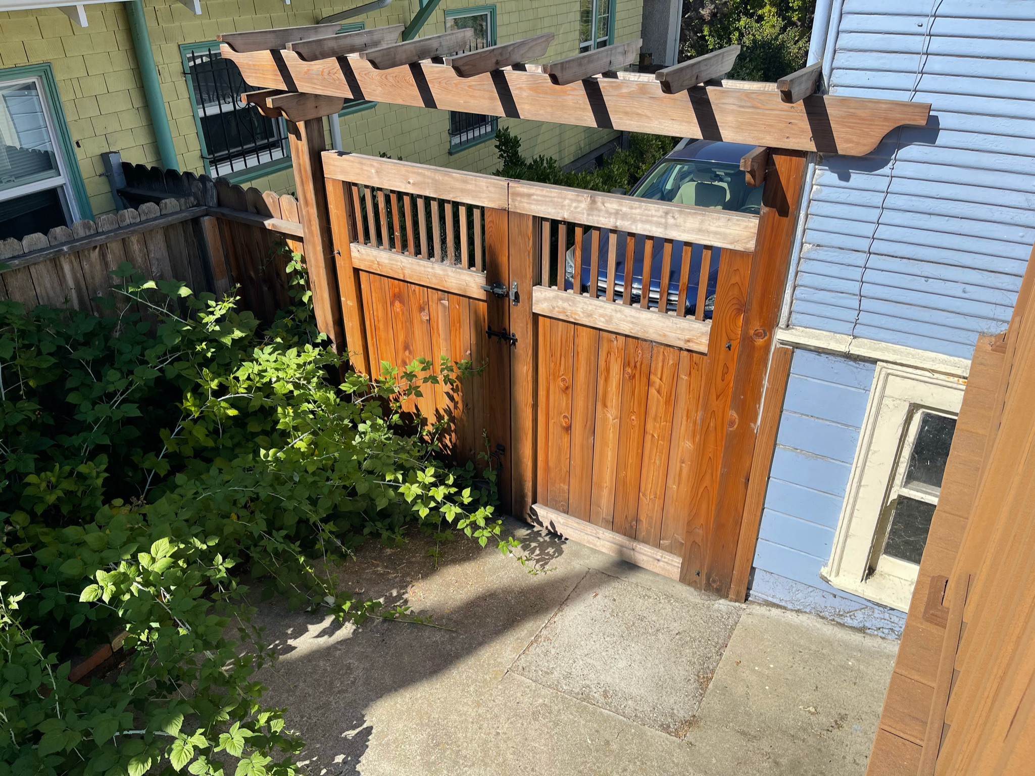 Sturdy wooden gate with pergola top provides secure access to front yard; adjacent concrete area allows for versatile landscaping.