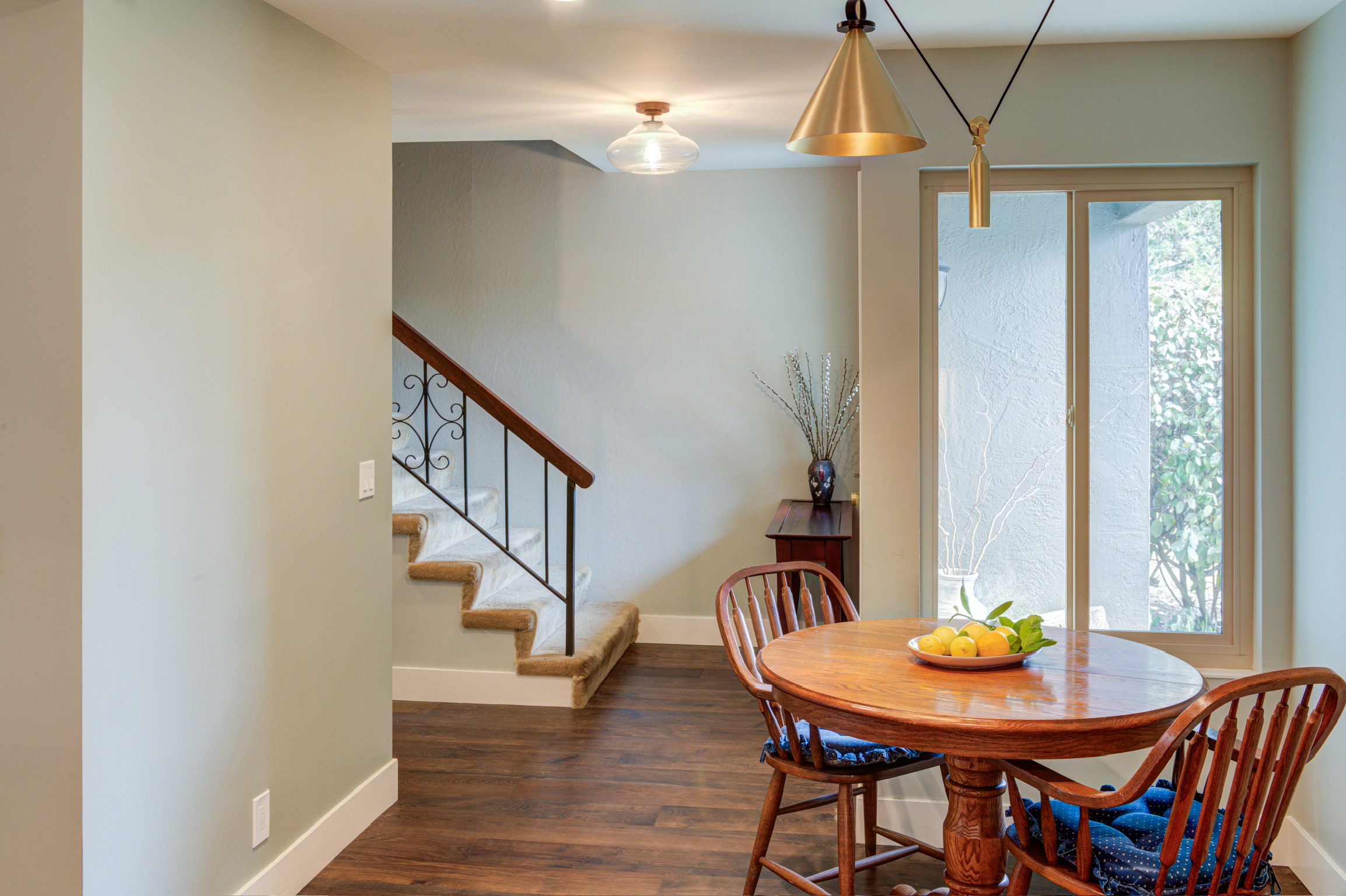 Open dining area beside large window, adjacent staircase with wooden handrail, layout highlighting optimal use of interior space.