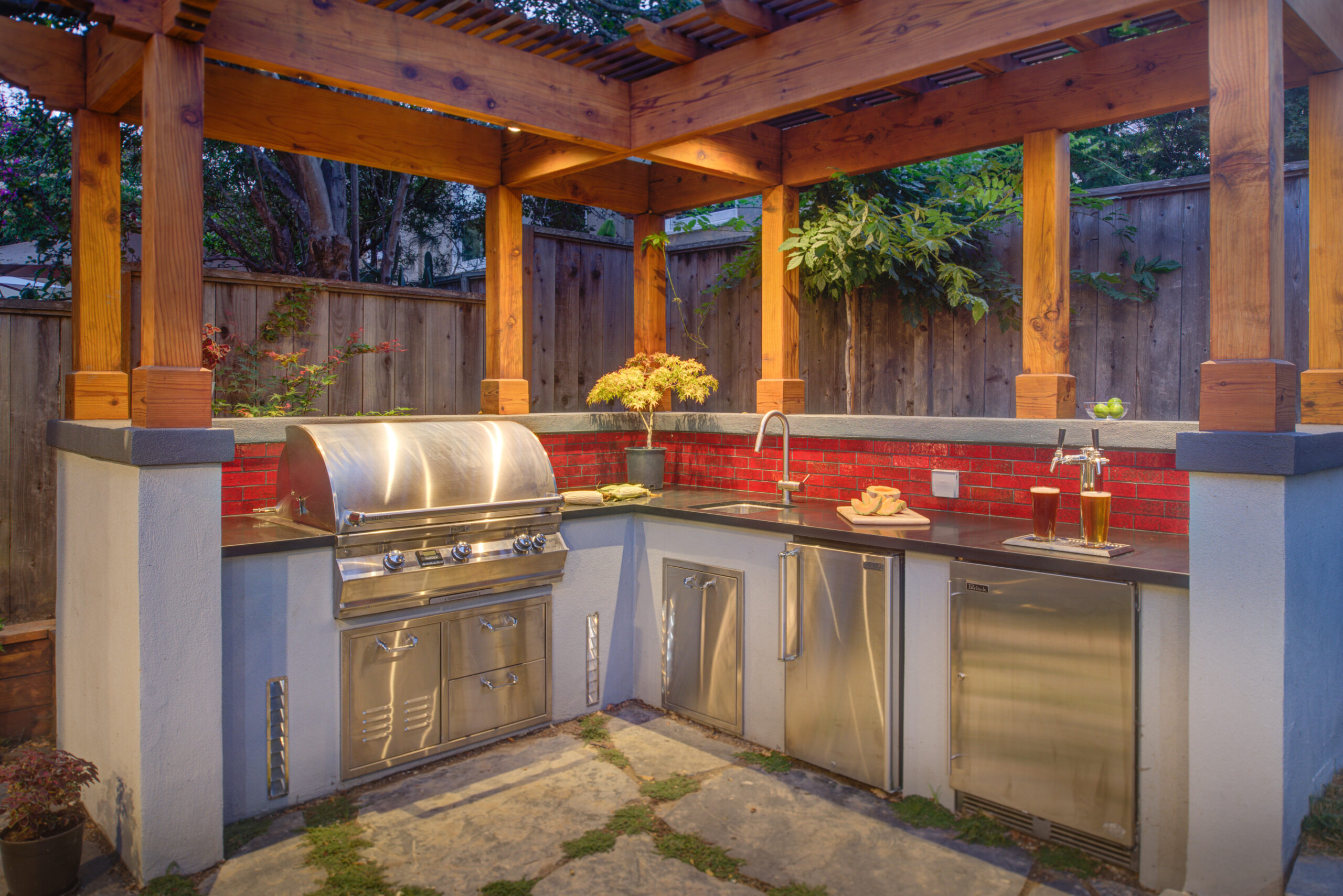 Outdoor kitchen in Oakland with durable appliances, built-in grill, sink, pergola structure, and stone patio ideal for remodeling.