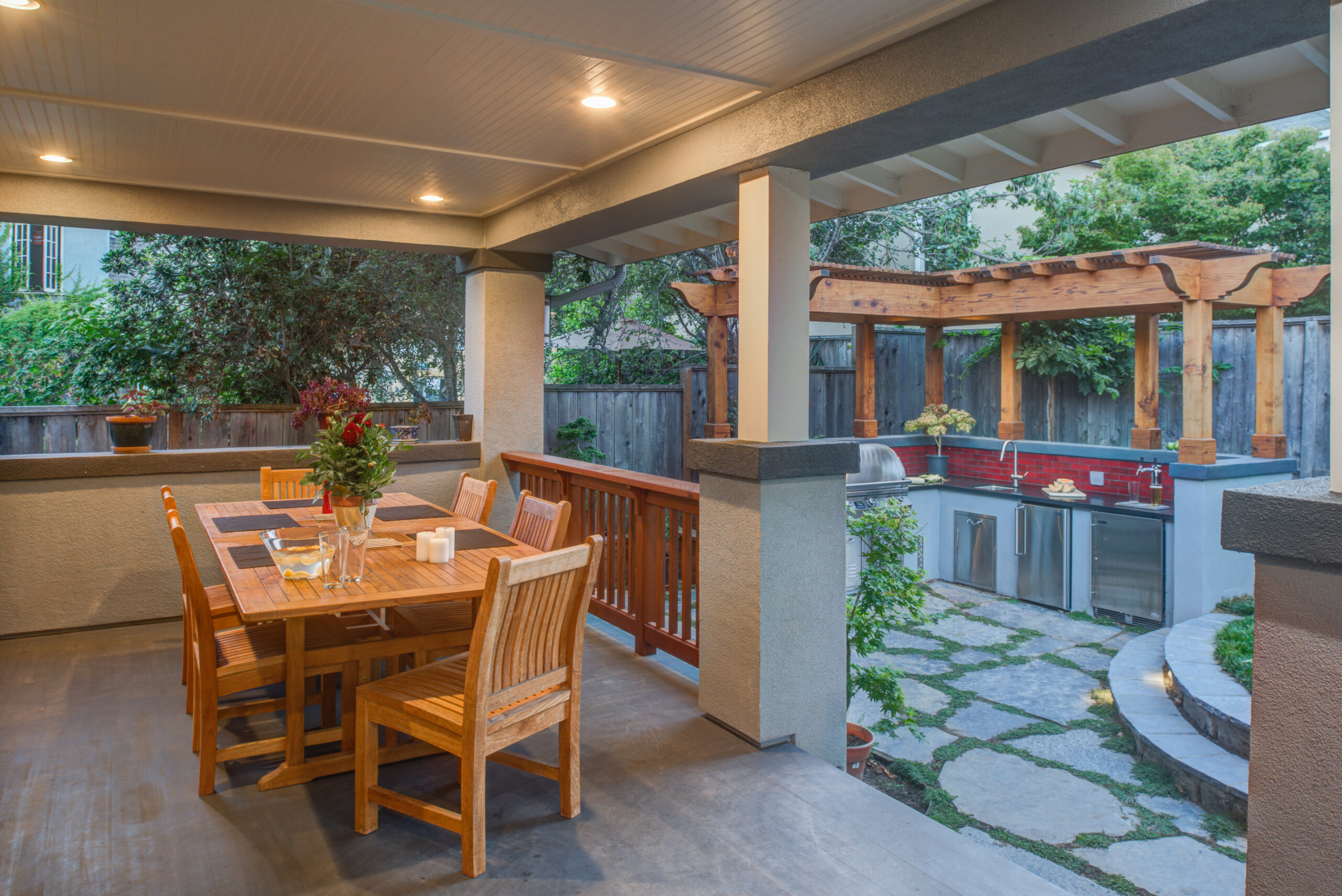 Covered patio overlooks an Oakland outdoor kitchen with pergola, stainless appliances, and functional stone pathway in landscaped yard.