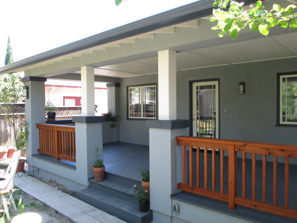 Porch with structural pillars, wood railing, glass-paneled entry door, and access to a large deck offering additional usable space.