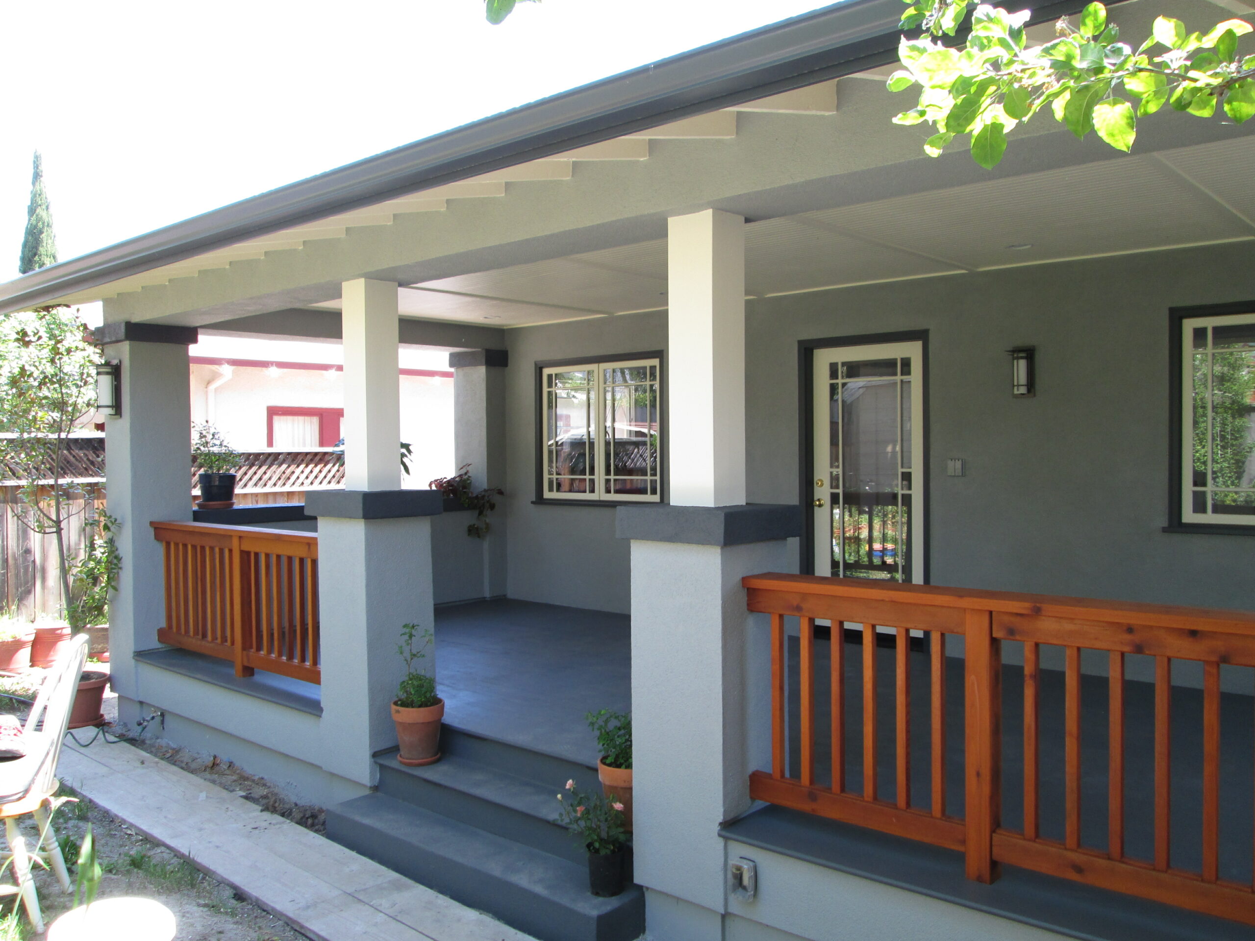 Porch with structural pillars, wood railing, glass-paneled entry door, and access to a large deck offering additional usable space.