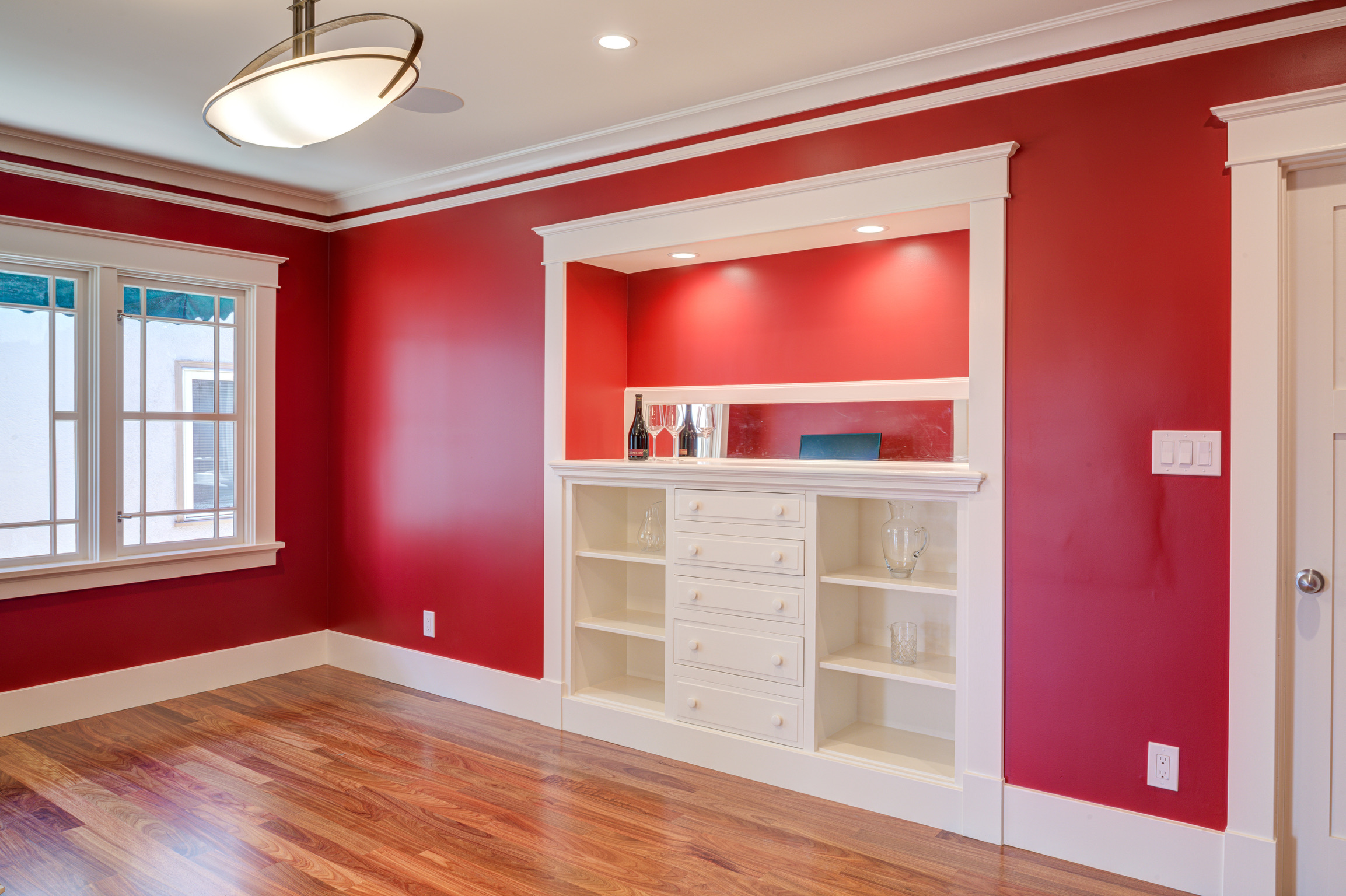 Room in Oakland with ample natural light, built-in shelving, hardwood flooring, large window, and overhead lighting—renovation potential.