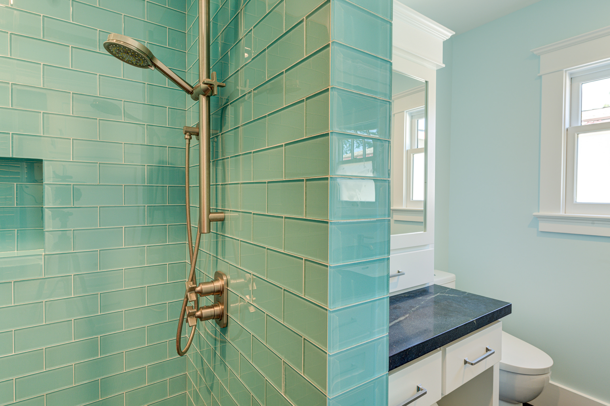 Modern shower with updated tiled walls, efficient fixtures, and visible plumbing access alongside vanity, toilet, and window.