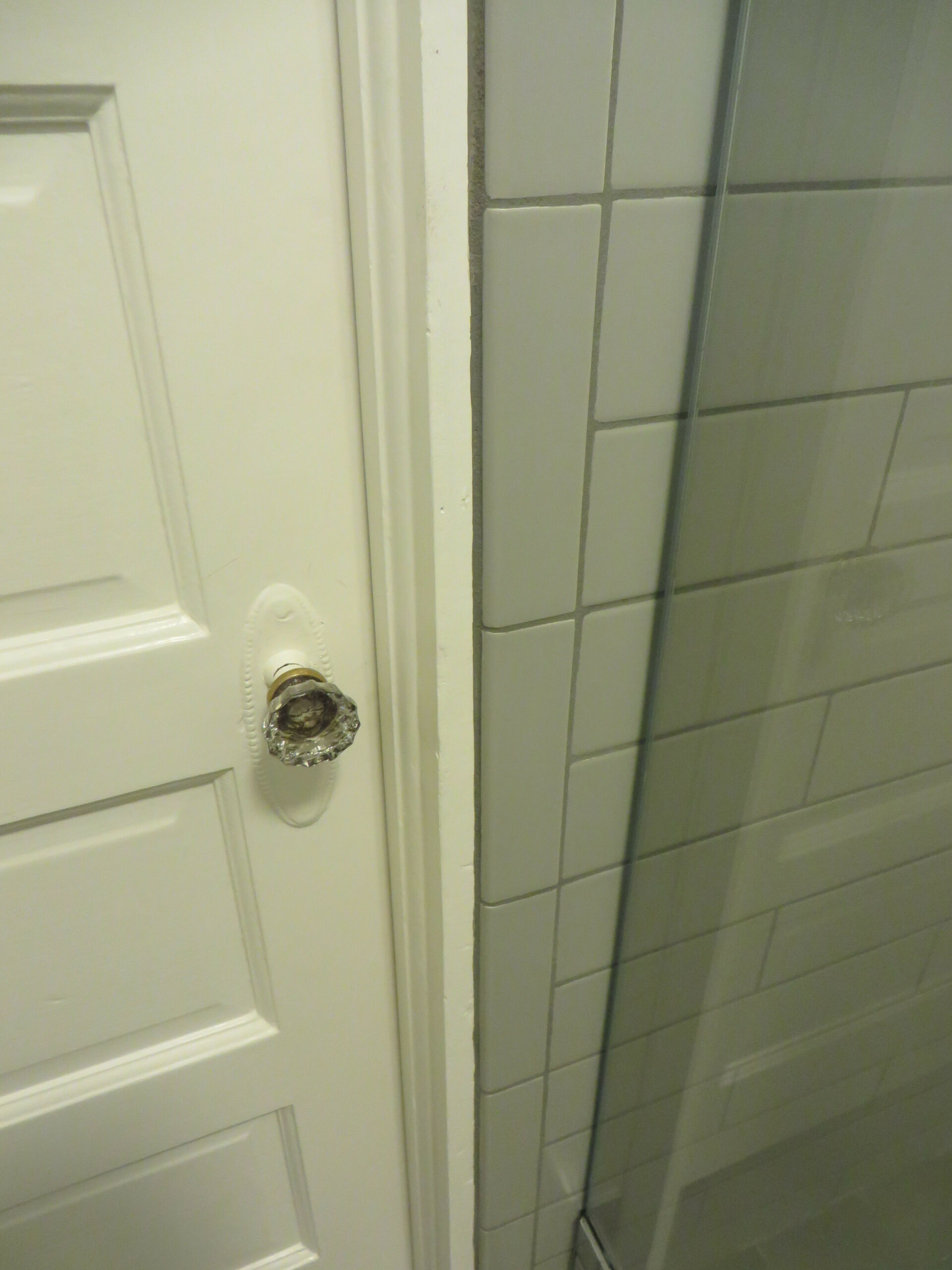 Interior bathroom door with missing or damaged doorknob near tiled wall and glass shower, indicating repair or replacement needs.