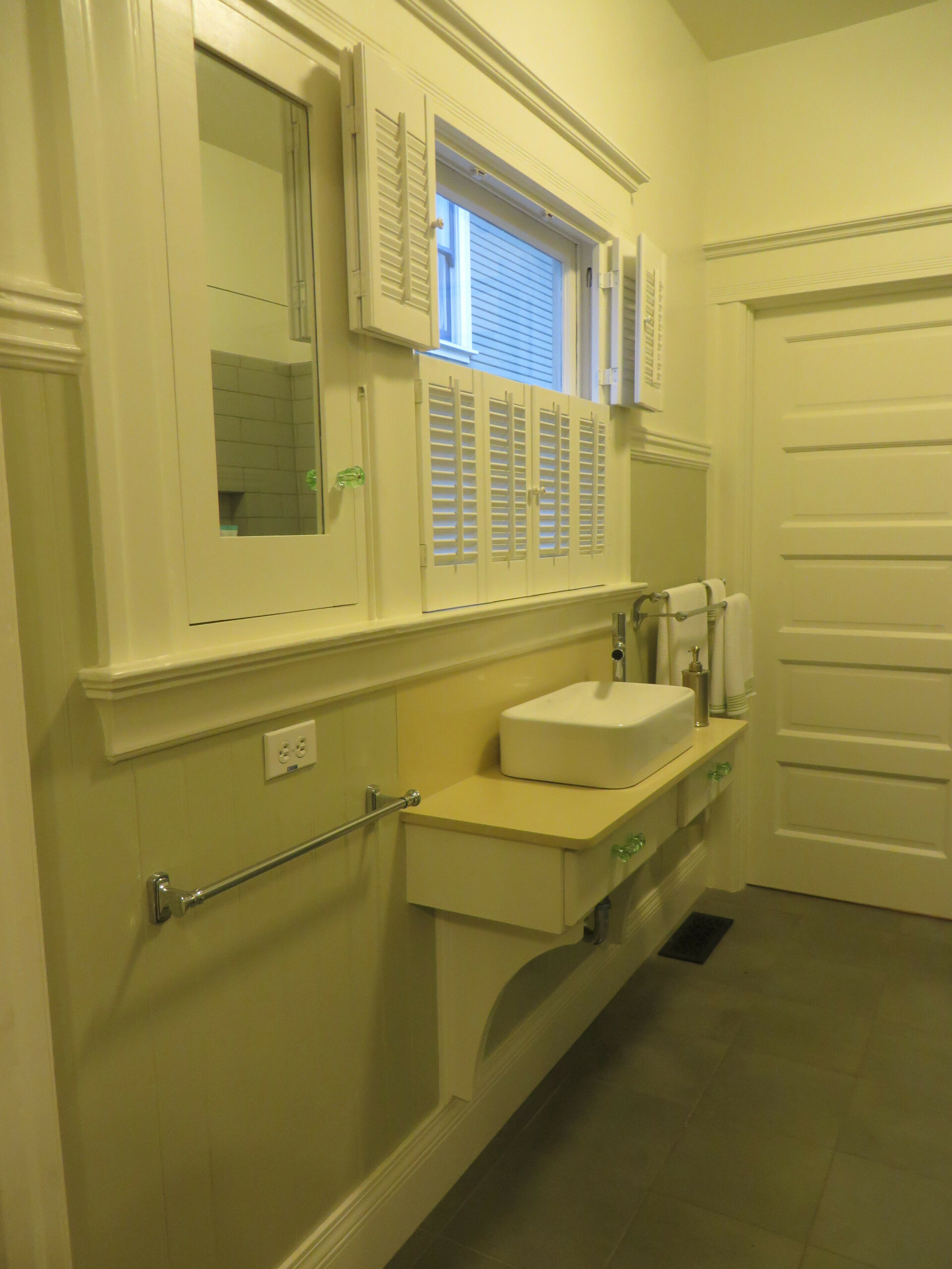 Piedmont Bathroom with wall-mounted sink, mirror cabinets, window with shutters, towel bar; efficient layout and durable tile flooring.