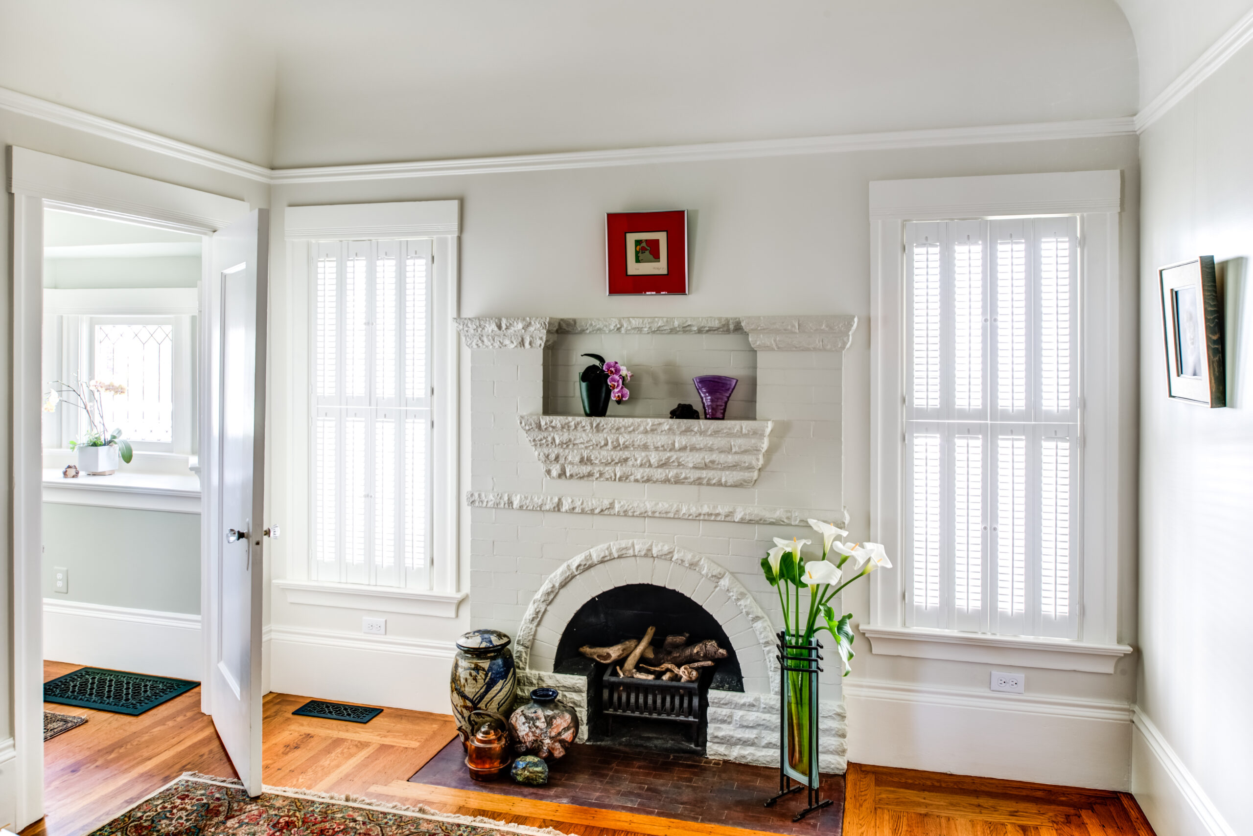 A remodeled brick fireplace serves as a focal point in a room with hardwood floors and energy-efficient shuttered windows.