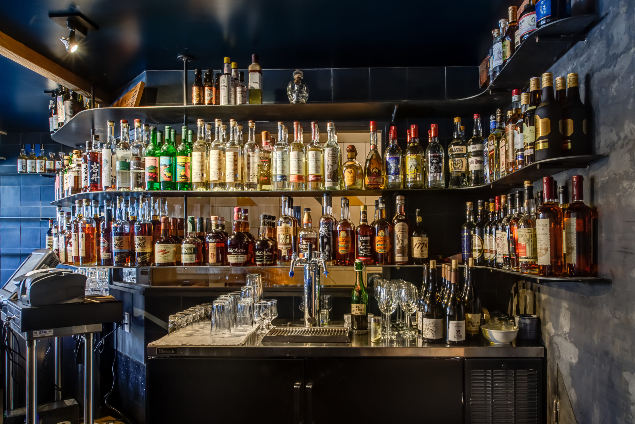 Bar setup with wall-mounted shelving, under-counter storage, built-in sink, and integrated beer tap—efficient for food service use.