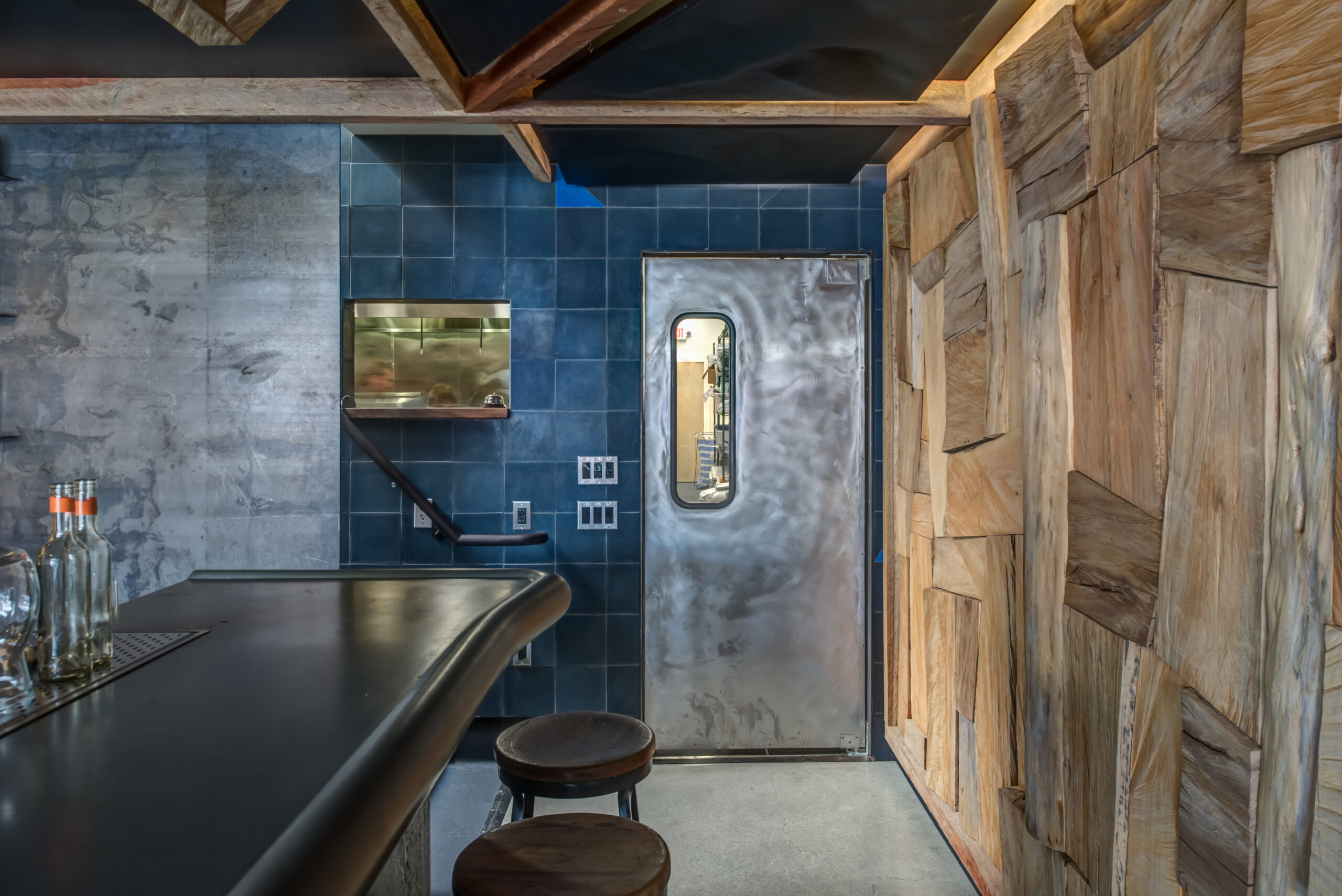 A metal door with a small window is built into a durable wall alongside wood paneling, showing mixed-material renovations.