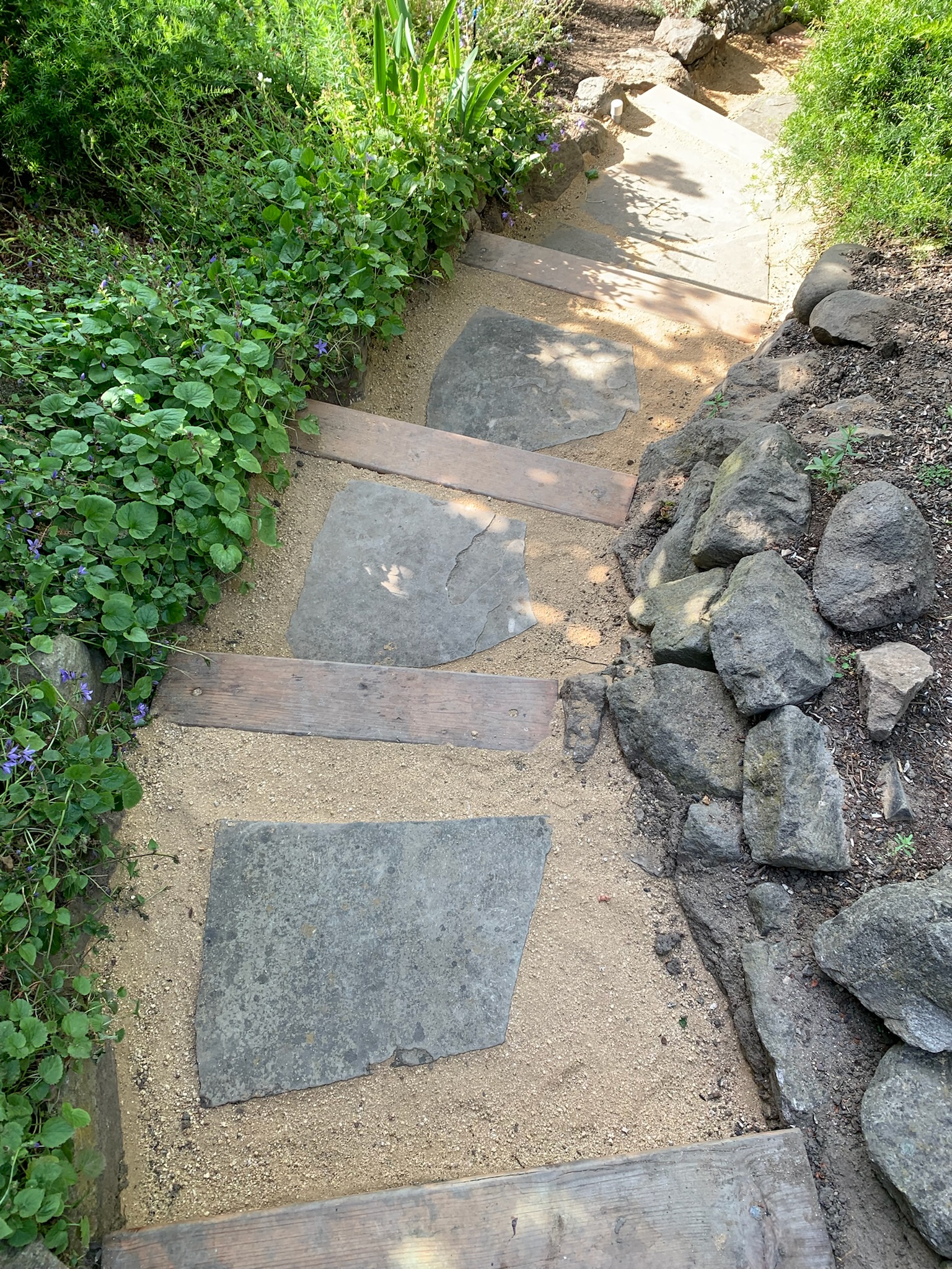 Backyard path with durable flat stone and wood construction, set in sand for drainage, bordered by low-maintenance landscaping.