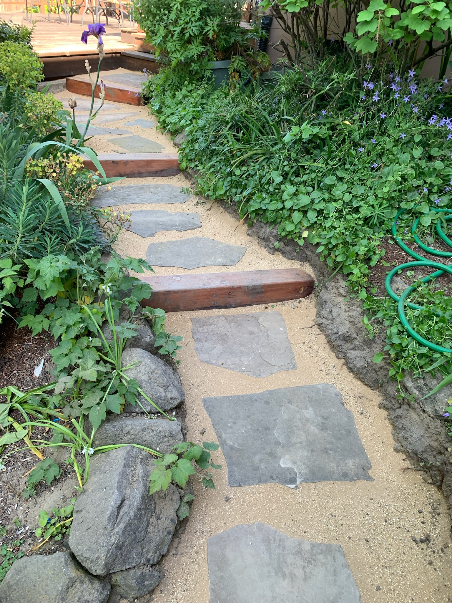 A durable stone pathway with integrated wooden steps winds through a spacious backyard, offering strong landscaping potential.