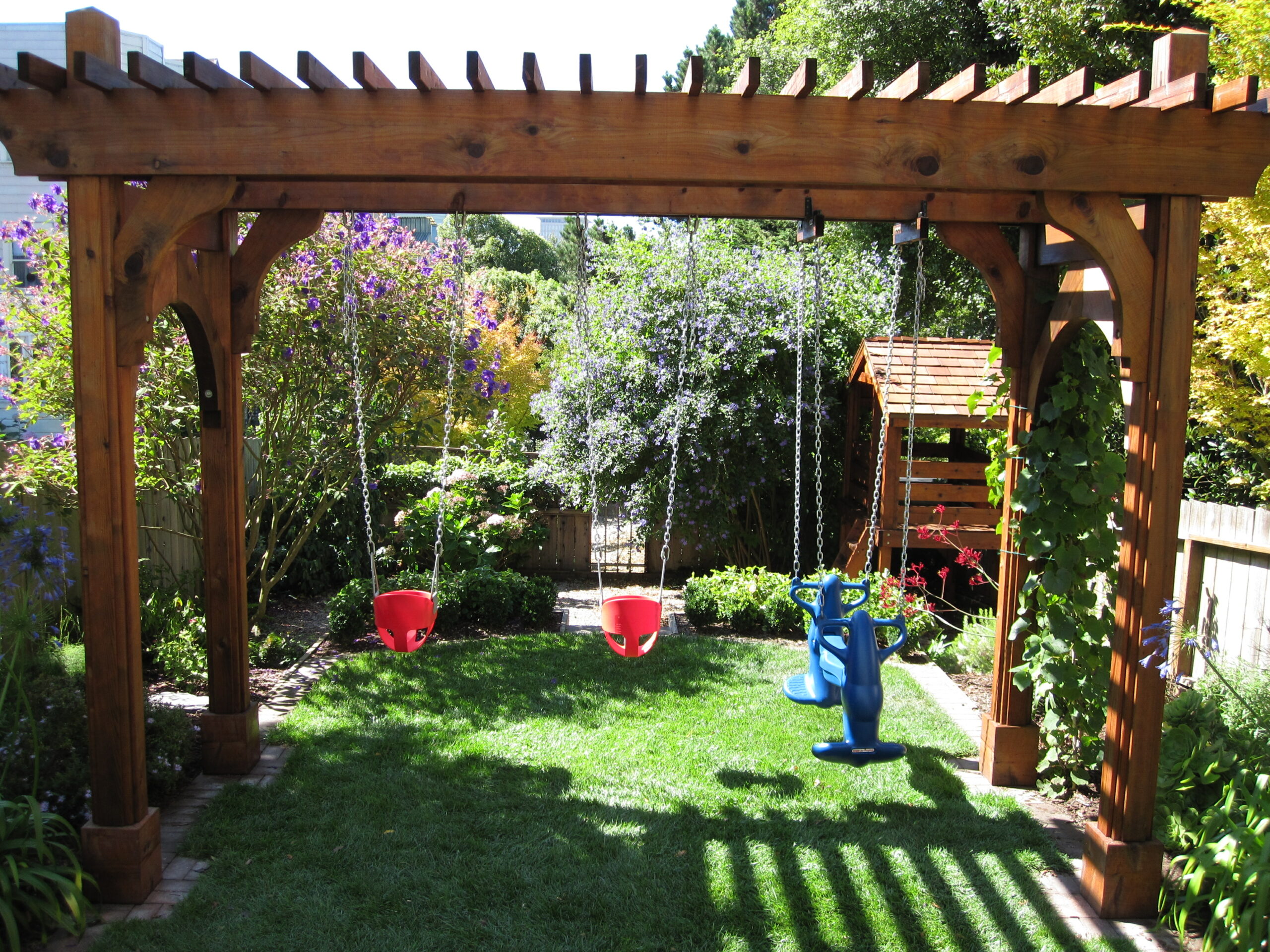 Sturdy wooden pergola with built-in swing support sits on grass, framed by mature landscaping in a San Francisco backyard.