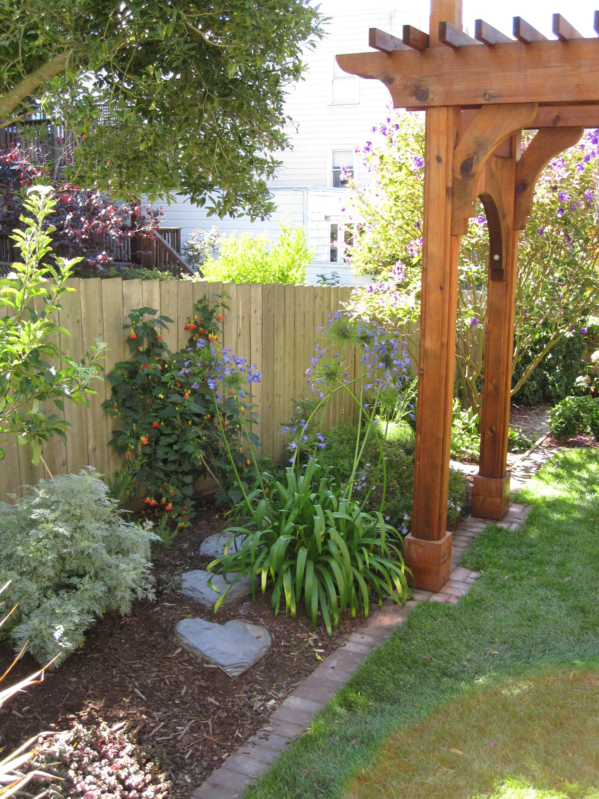 Wooden pergola next to established garden bed, hardscape pathway, and privacy fencing in a functional San Francisco backyard.