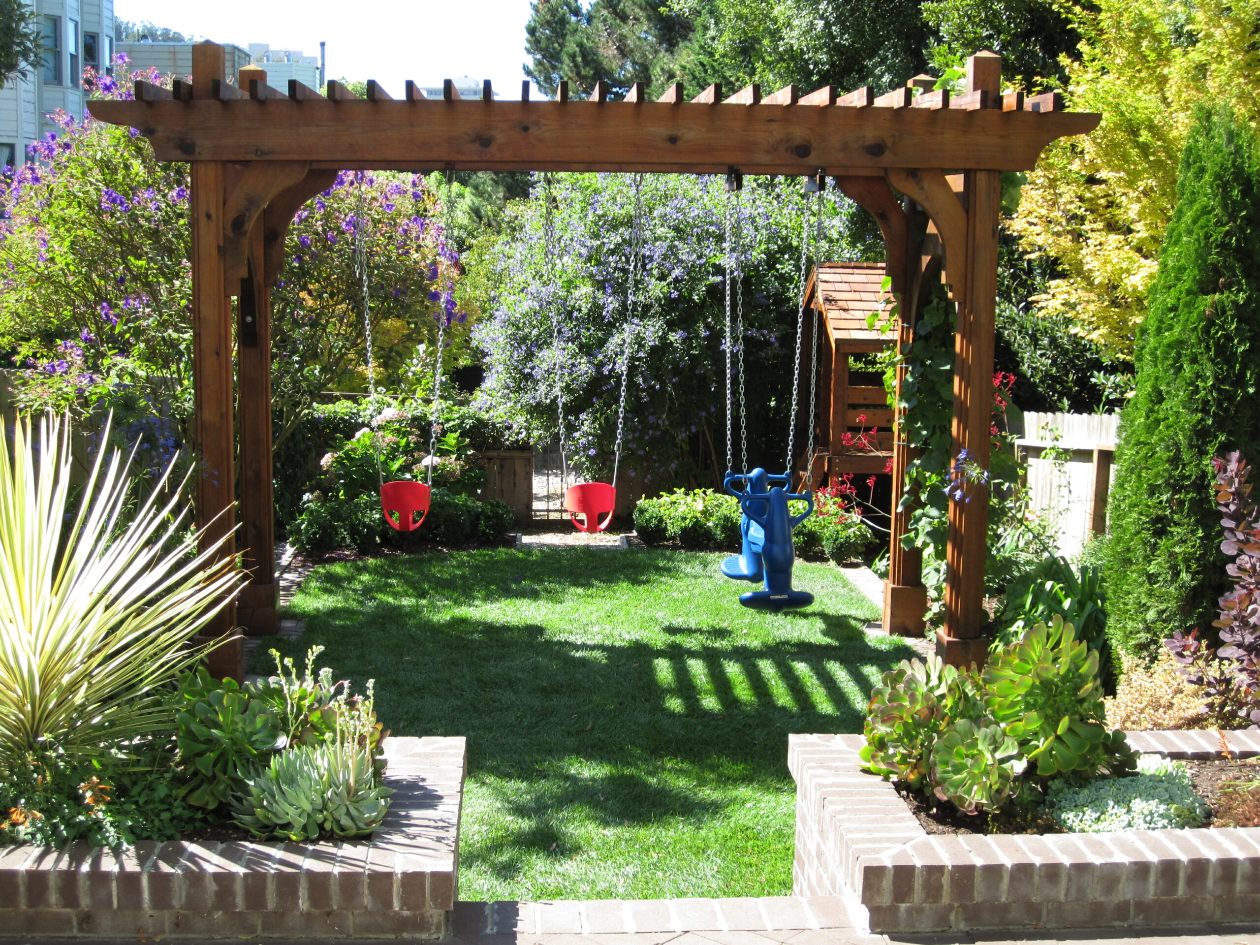 A wooden pergola defines a usable backyard space in San Francisco, featuring play equipment and mature landscaping.