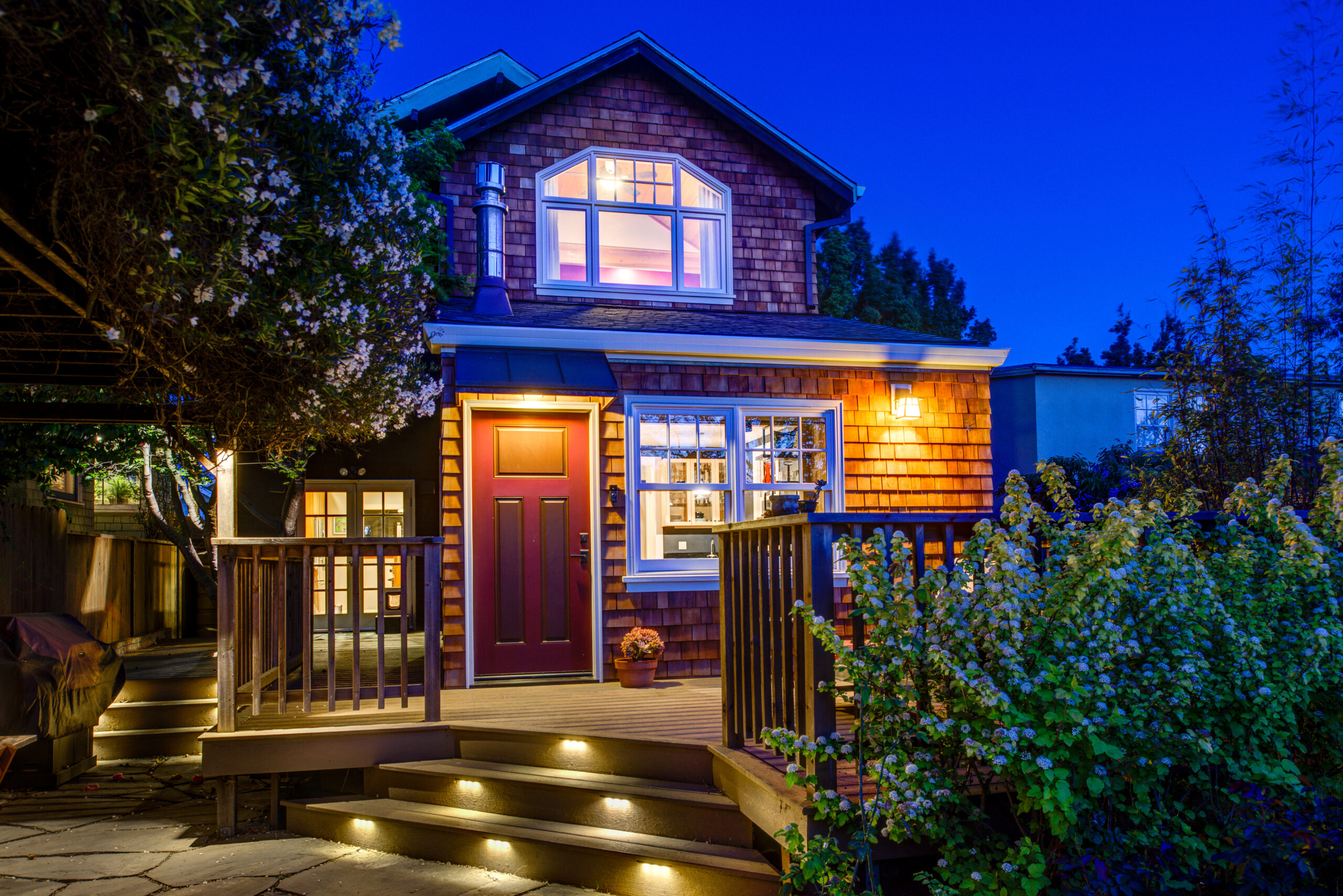 Two-story Temescal house with wood siding, large windows, and porch access; well-lit entry steps overlook a private backyard.