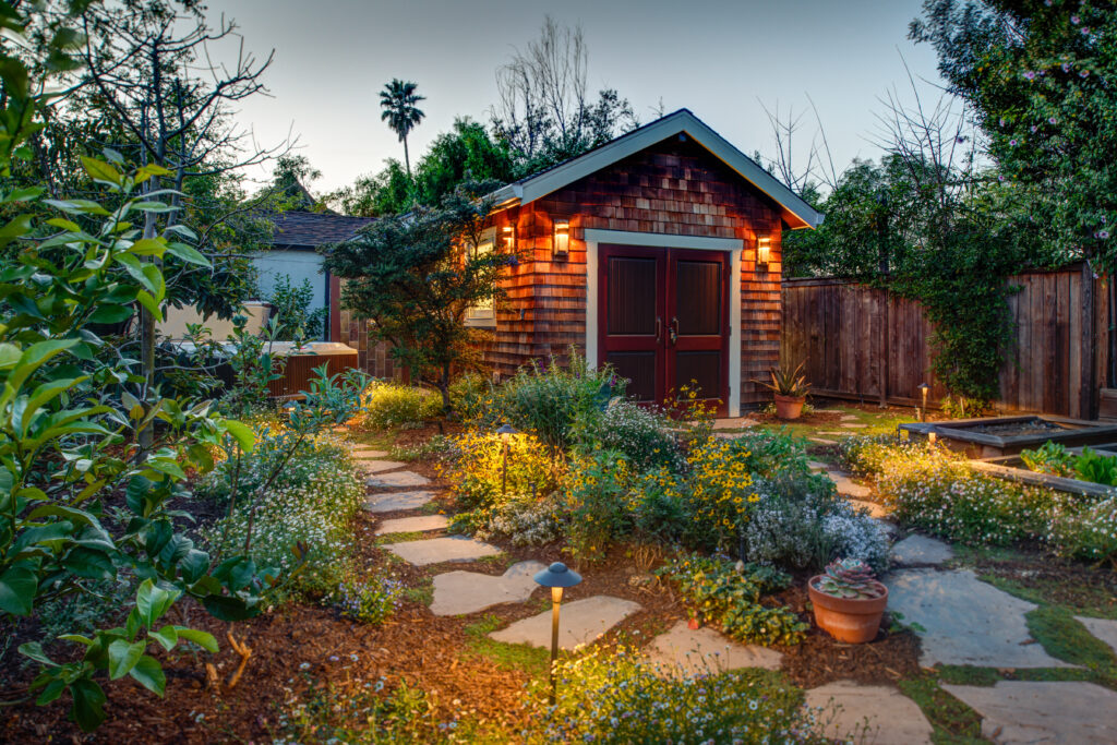 Compact backyard shed with double doors and exterior lighting, situated near stone pathways; ample space for landscaping upgrades.