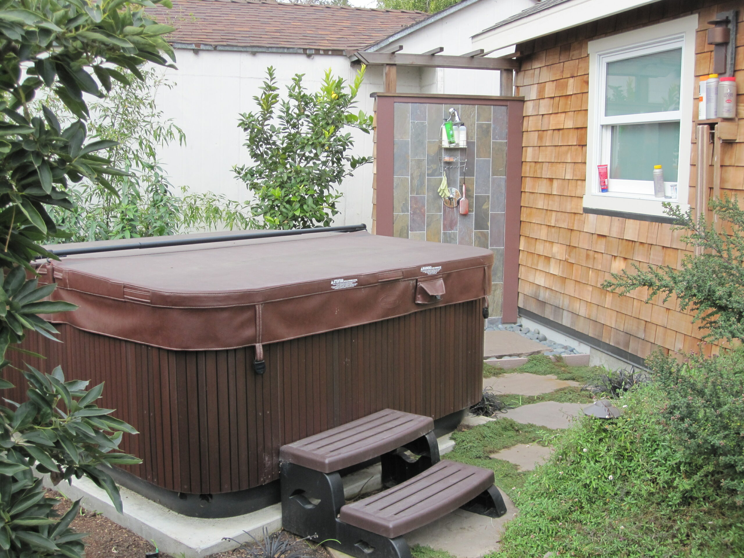 Outdoor hot tub with steps and stone-tiled shower installed in backyard, highlighting potential for modern amenities and upgrades.