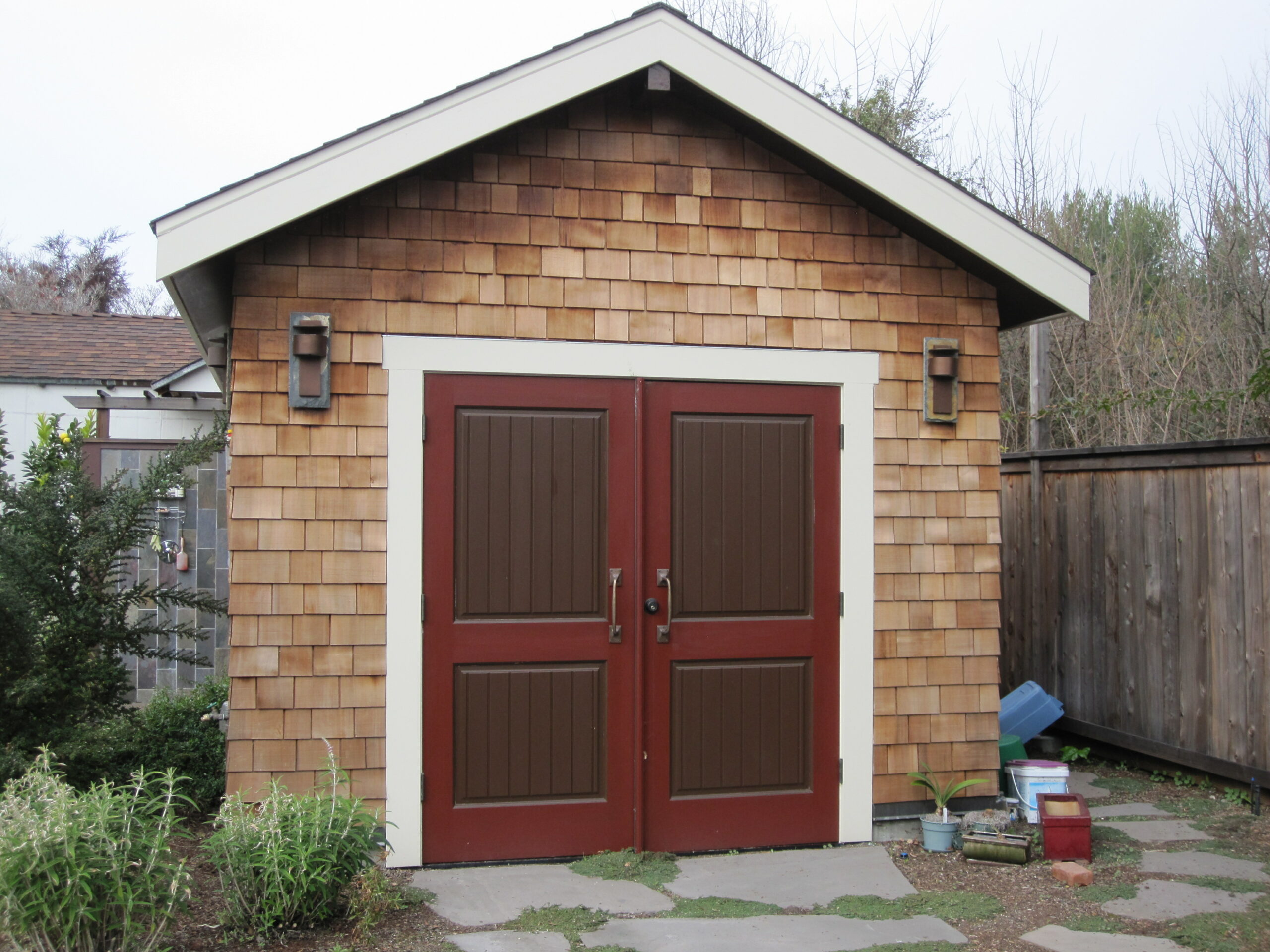 Small wooden shed with double doors and exterior lighting, suitable for backyard use and potential redevelopment or storage.