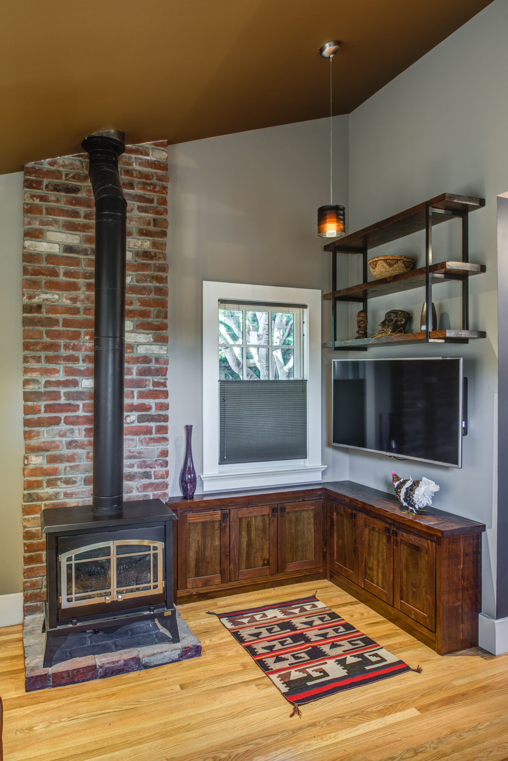 Corner living space features wood-burning stove, exposed brick chimney, built-ins, and efficient layout—potential for renovation.