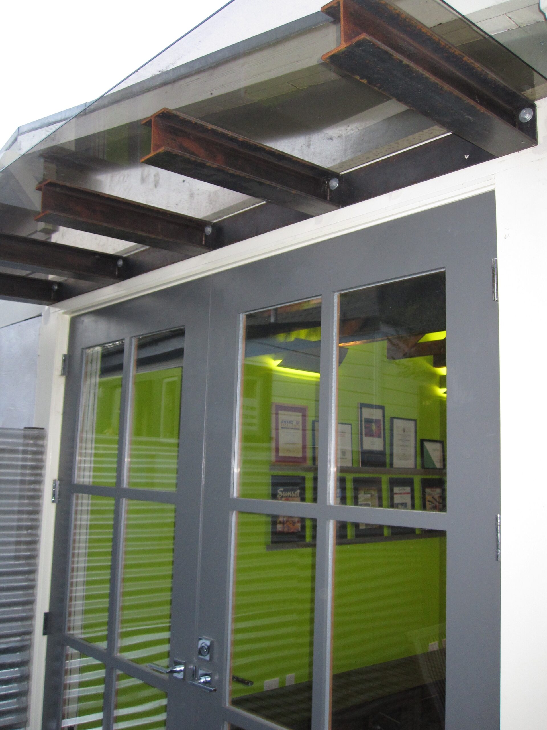 Double glass entry doors beneath a sturdy awning lead to an office with open wall space and ample natural light, redevelopment potential.