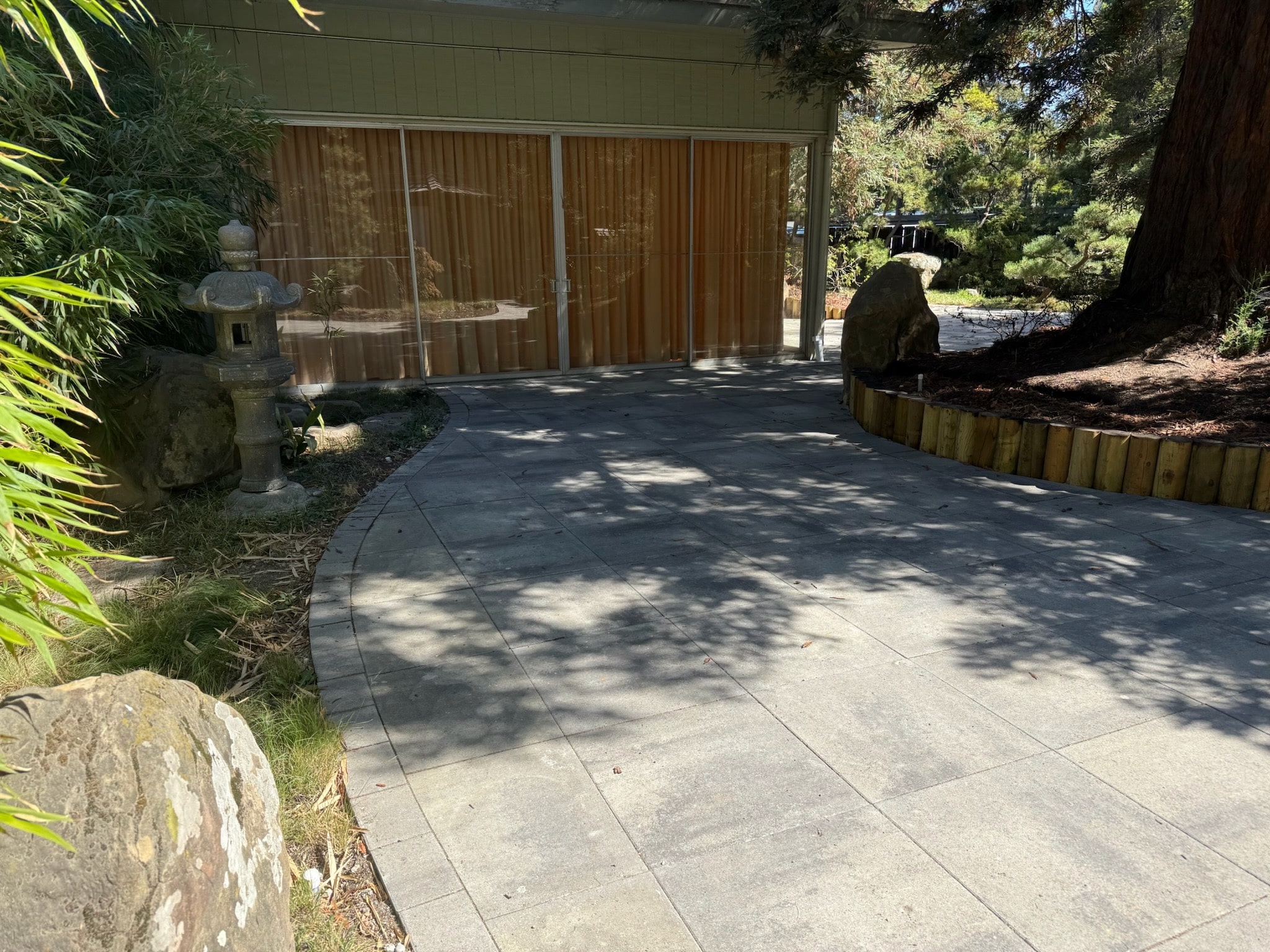 A stone patio with curved edge and landscaped borders sits adjacent to large glass doors, offering indoor-outdoor flow near Lake Merritt.